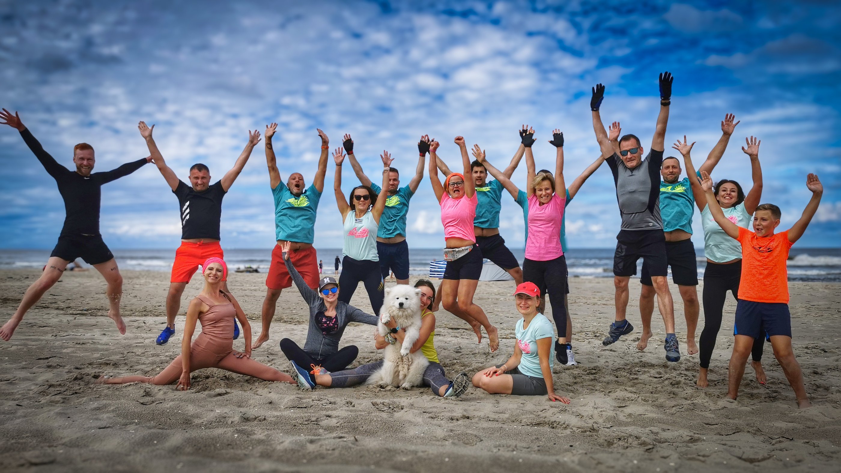 Uśmiechnięta grupa osób w podskoku na plaży po treningu. 