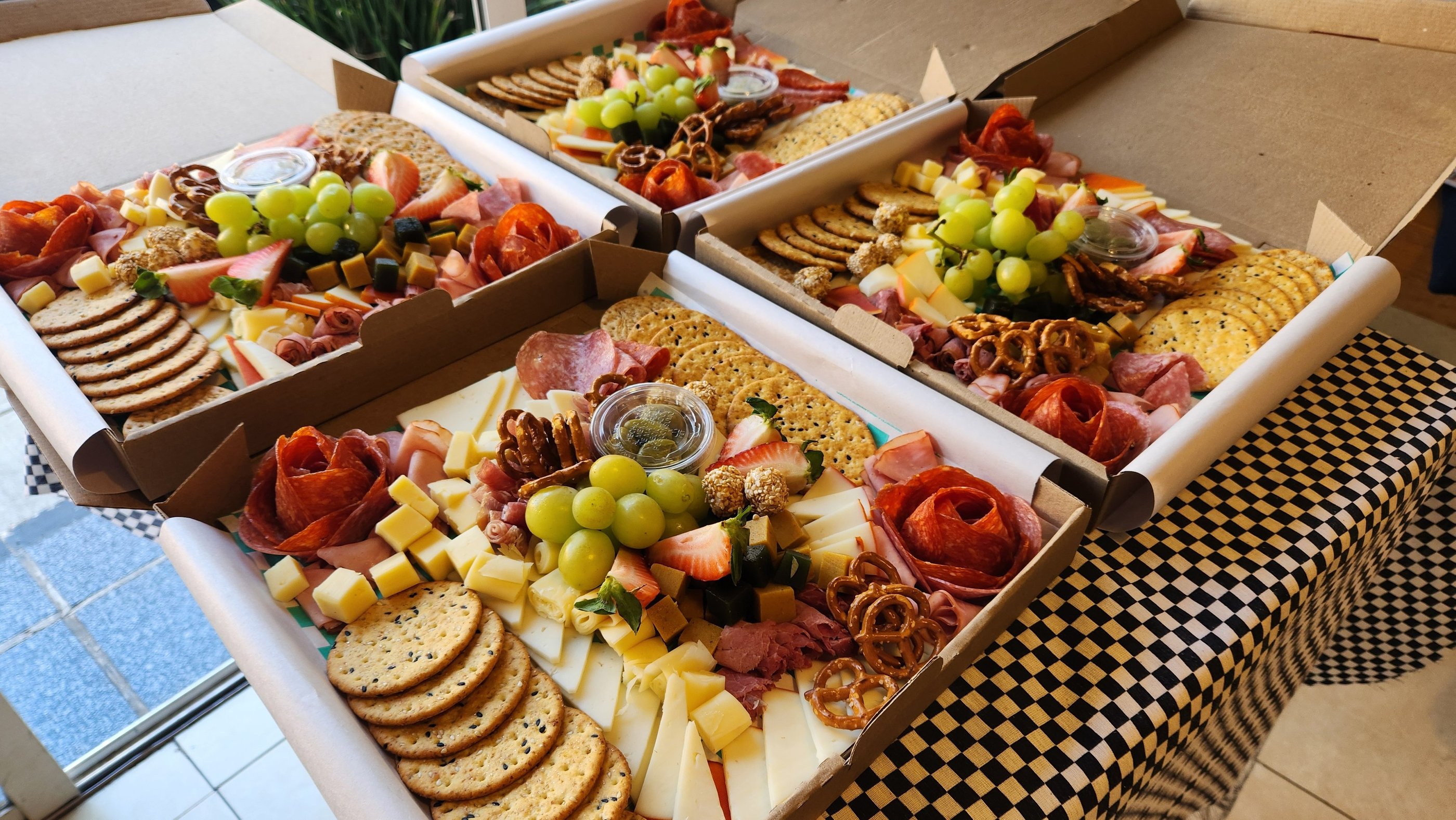 Gourmet charcuterie boxes with artisanal cheeses, salami roses, crackers, grapes, and pretzels.