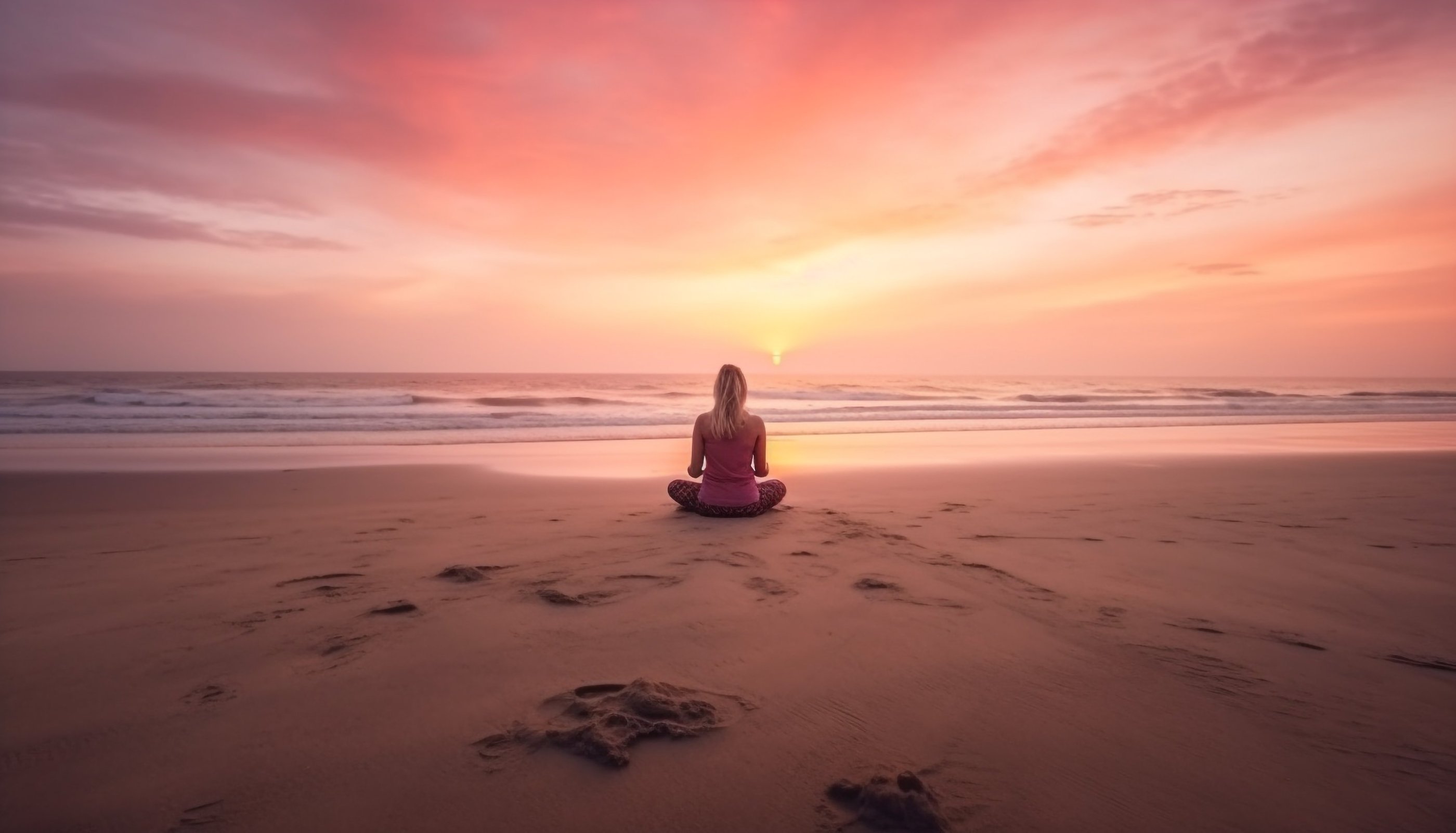 a woman sitting on a beach with a sunset in the background