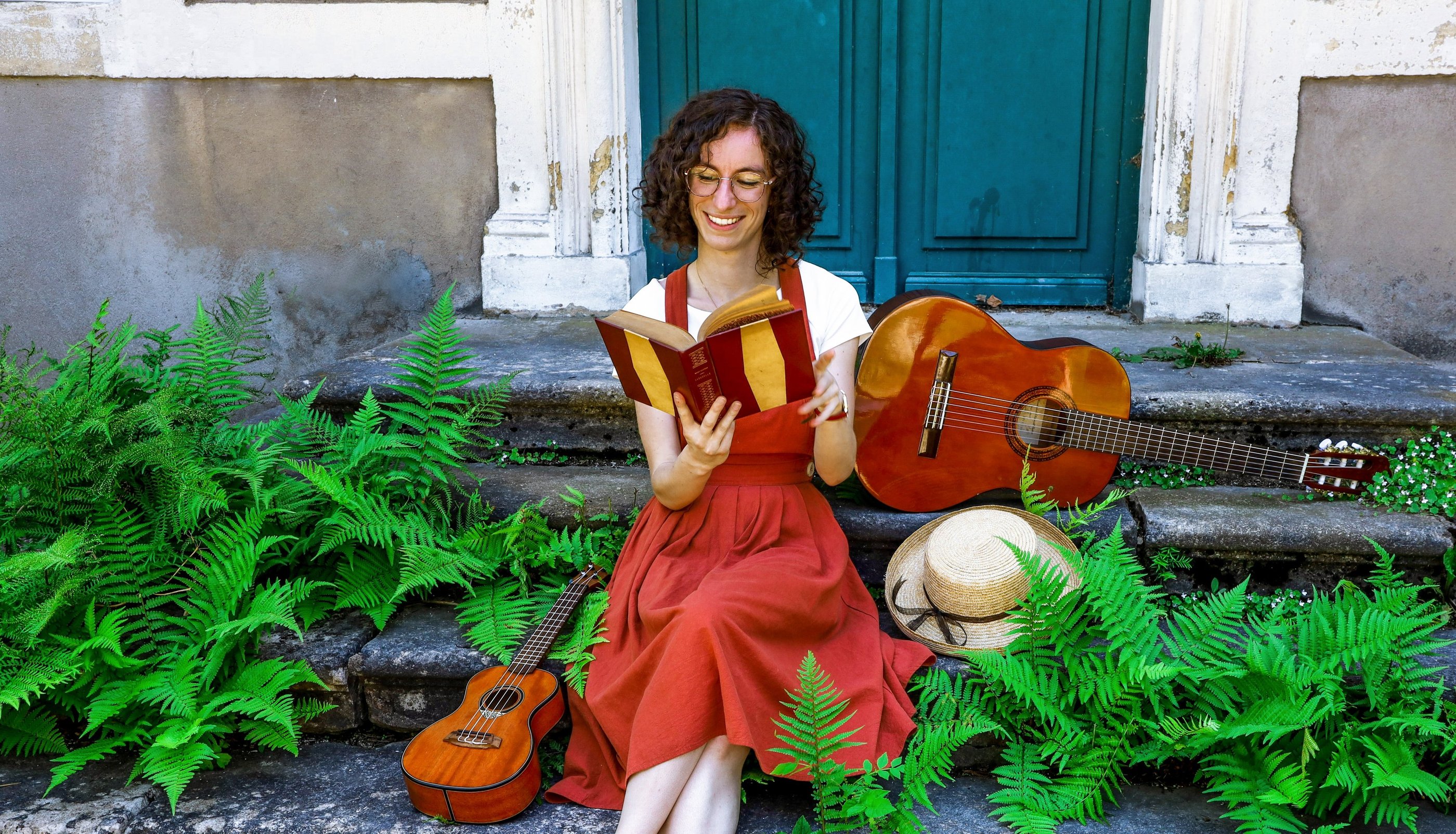 musicienne en train de lire un livre/a woman in a red dress reading on stairs with guitar beside her