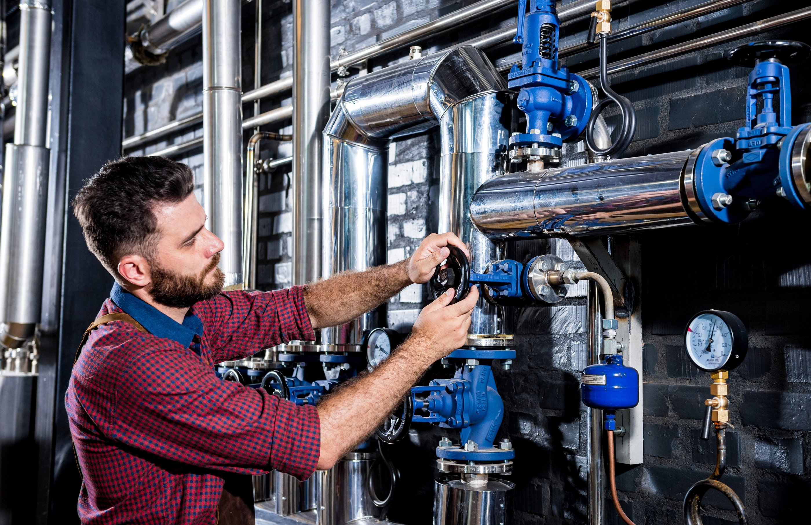 Técnico de mantenimiento con barba ajustando una válvula en tuberías industriales de acero