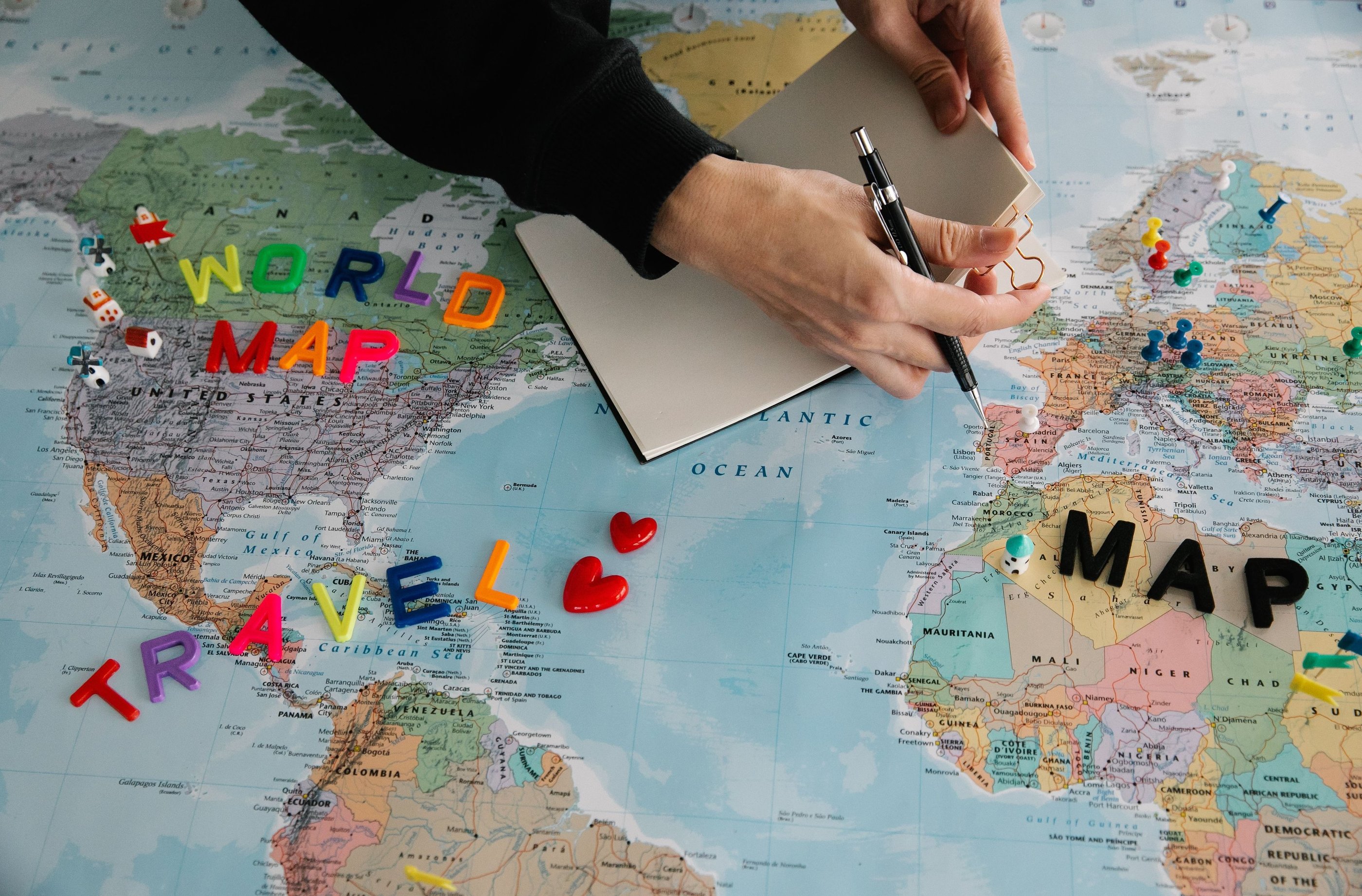 A person planning a trip on a world map with a notebook, pen, and colorful travel magnets.