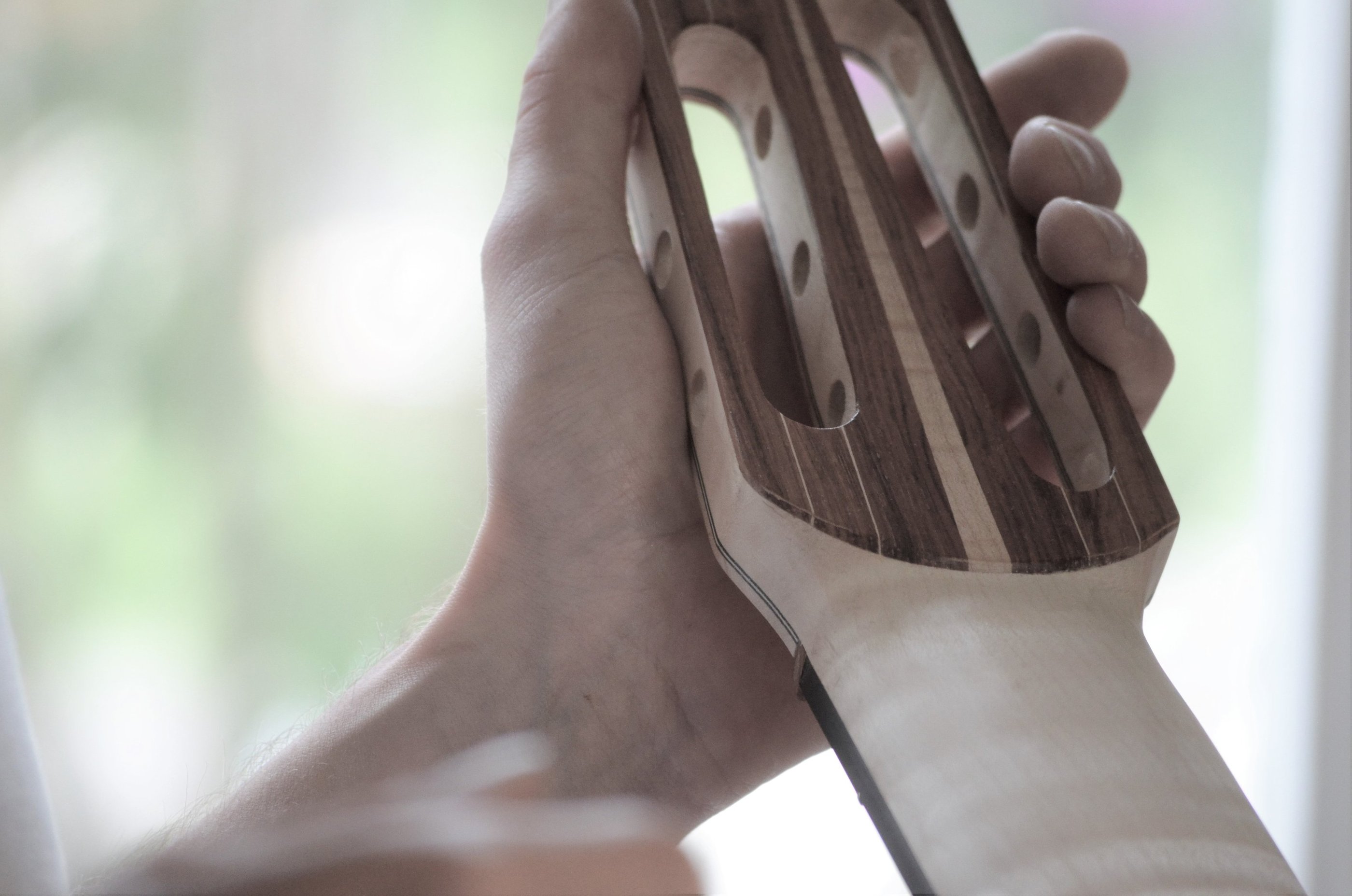 A luthier holding a handcrafted wooden 7 string guitar headstock during the assembly process.