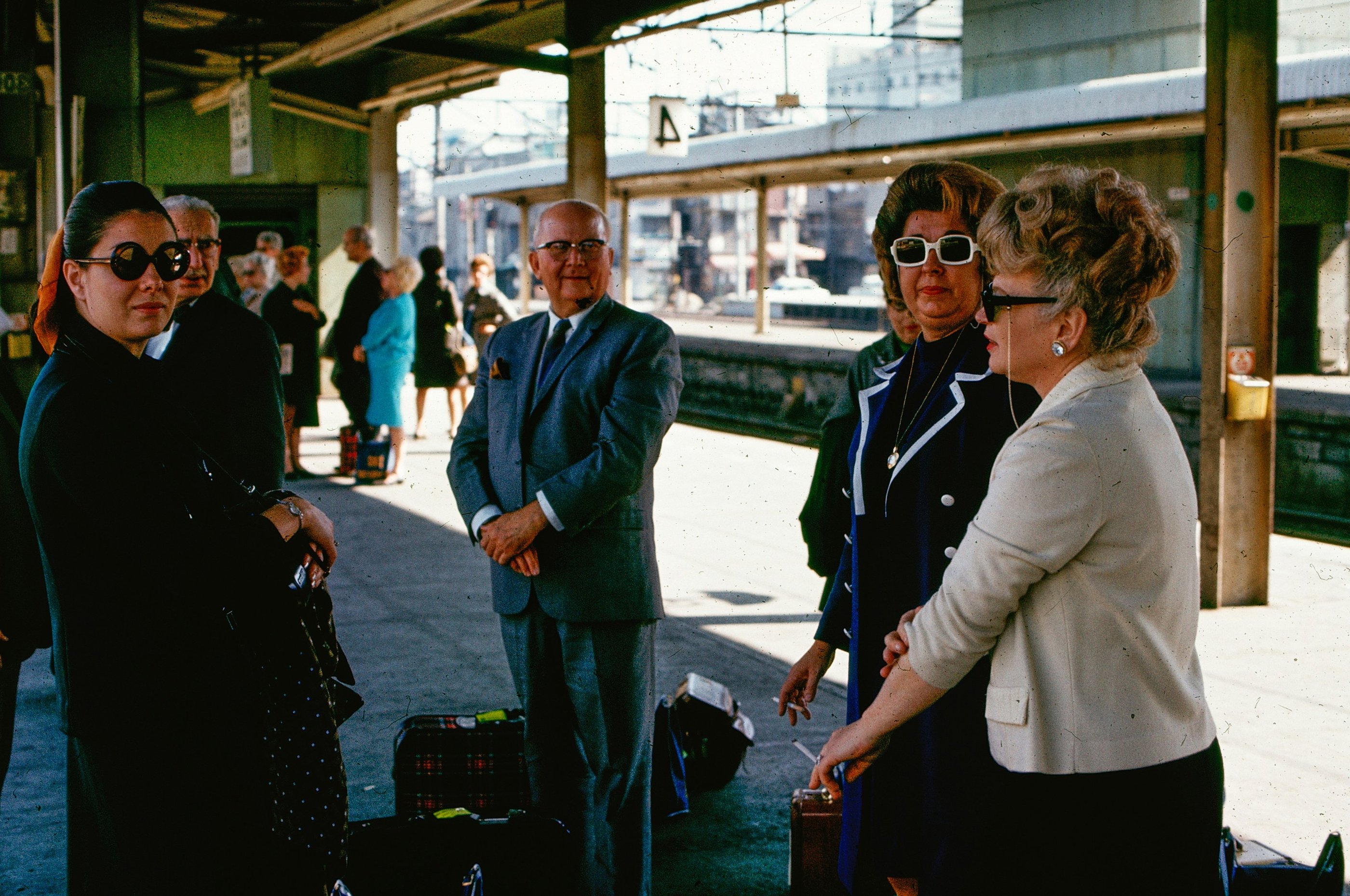 Vintage photo of stylish travelers wearing sunglasses at a train station platform in the 1960s.
