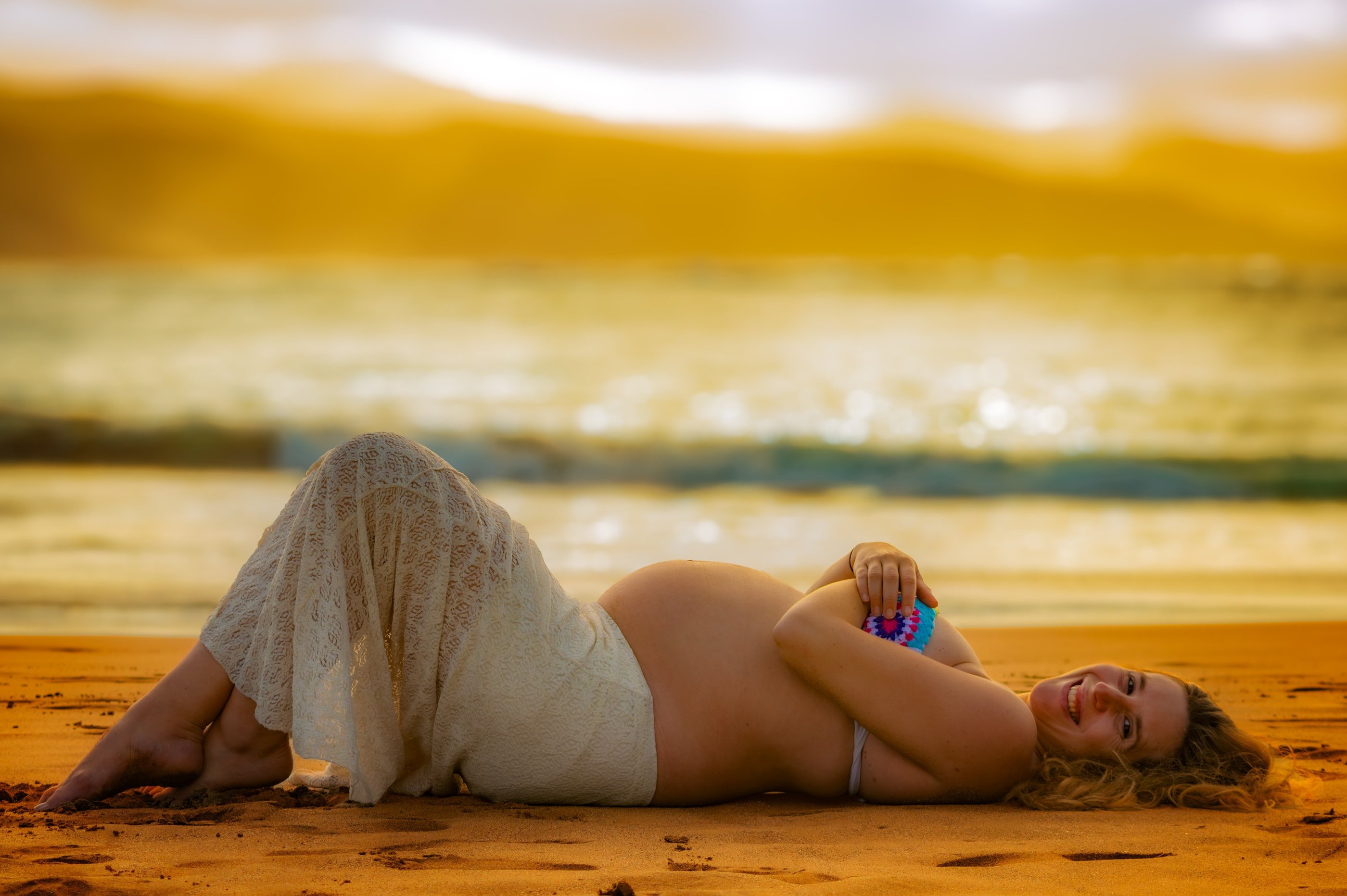 a pregnant woman laying on the beach