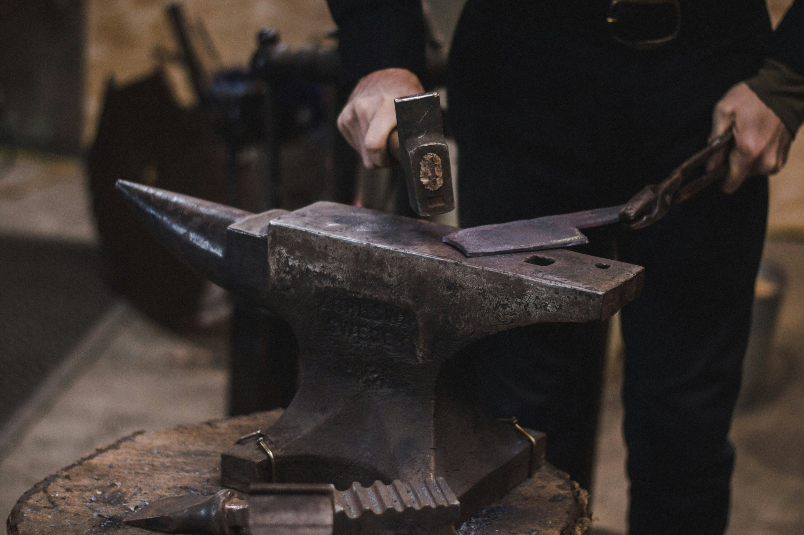 A blacksmith uses a forging hammer and tongs to shape hot metal on a traditional iron anvil.