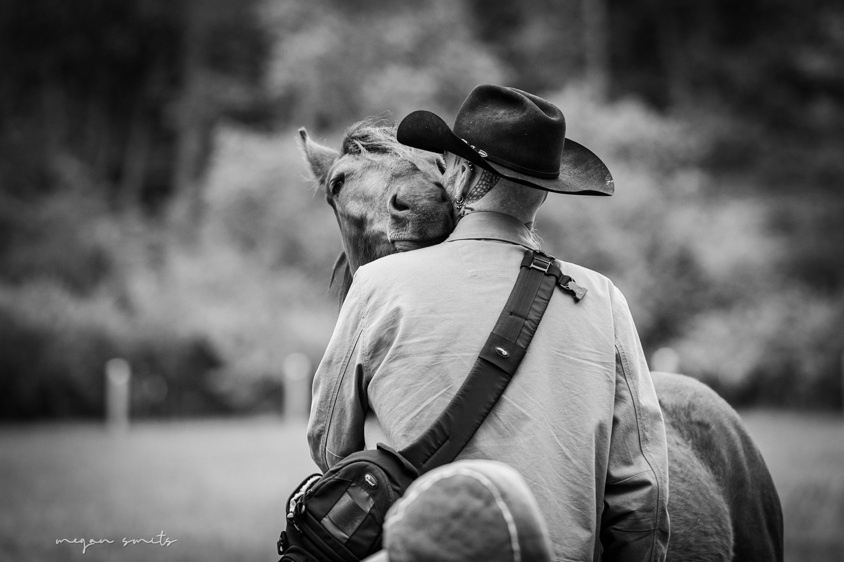A black and white photo showing Drake in a cowboy hat sharing an affectionate moment with a horse. 