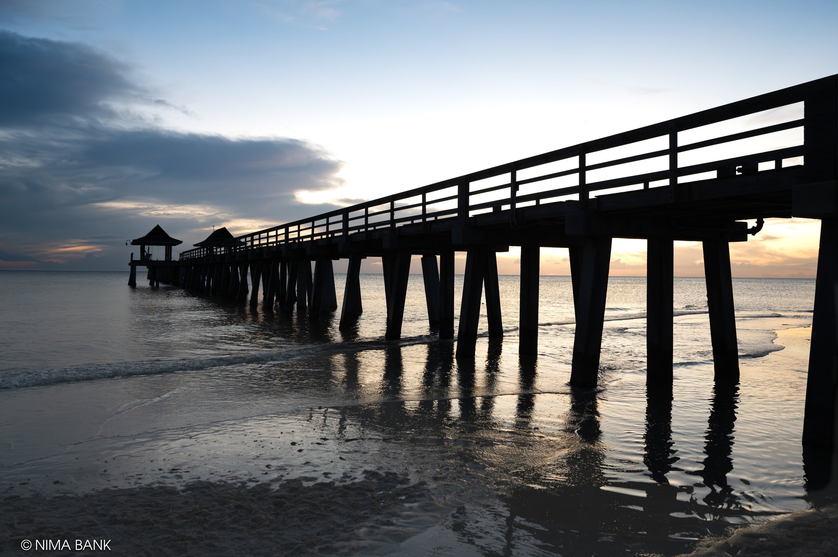 shadowy sunset view of naples pier in naples florida, with waves and the ocean and clouds 