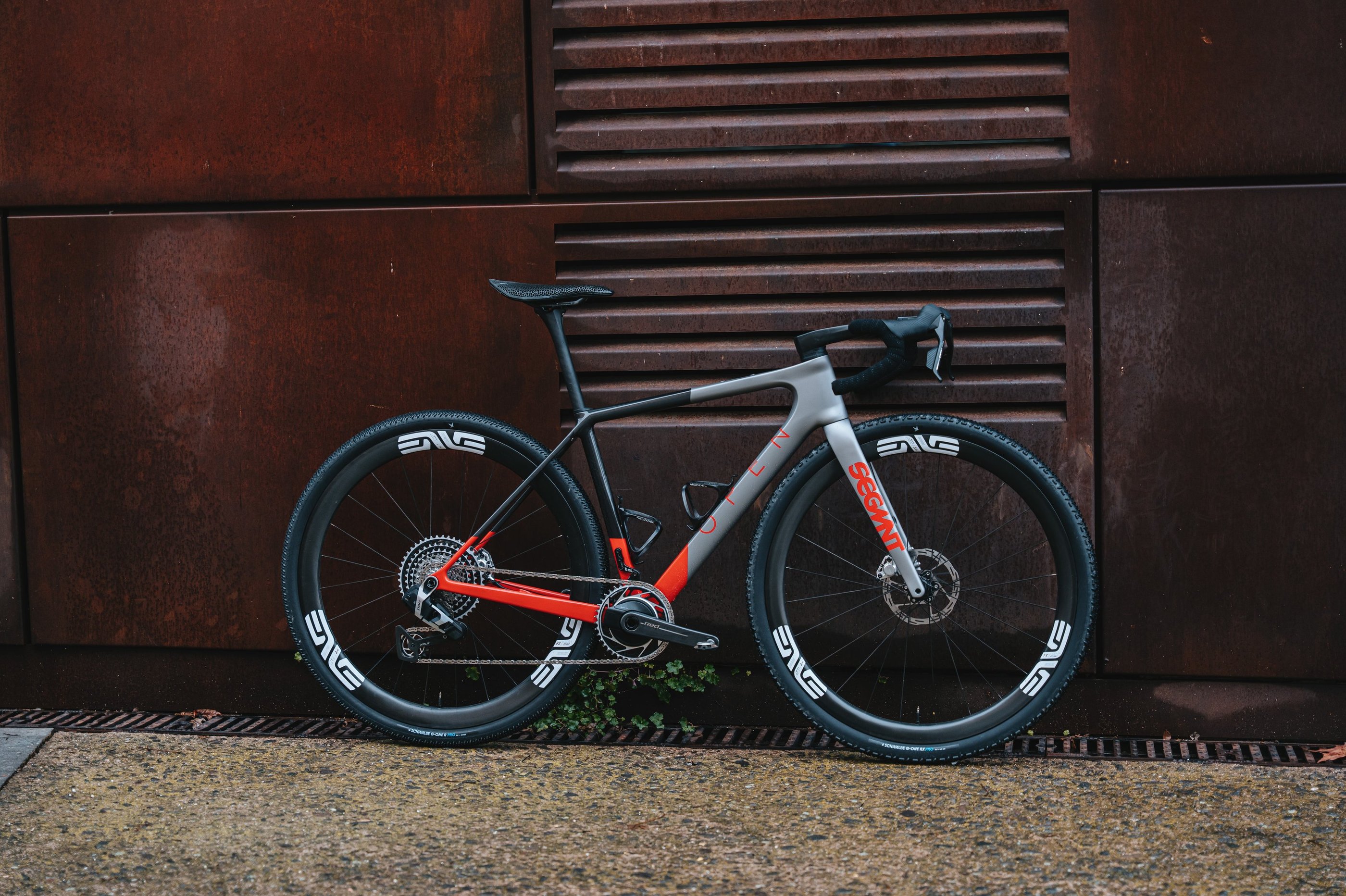 Custom OPEN gravel bike with ENVE carbon wheels leaning against a weathered metal wall.