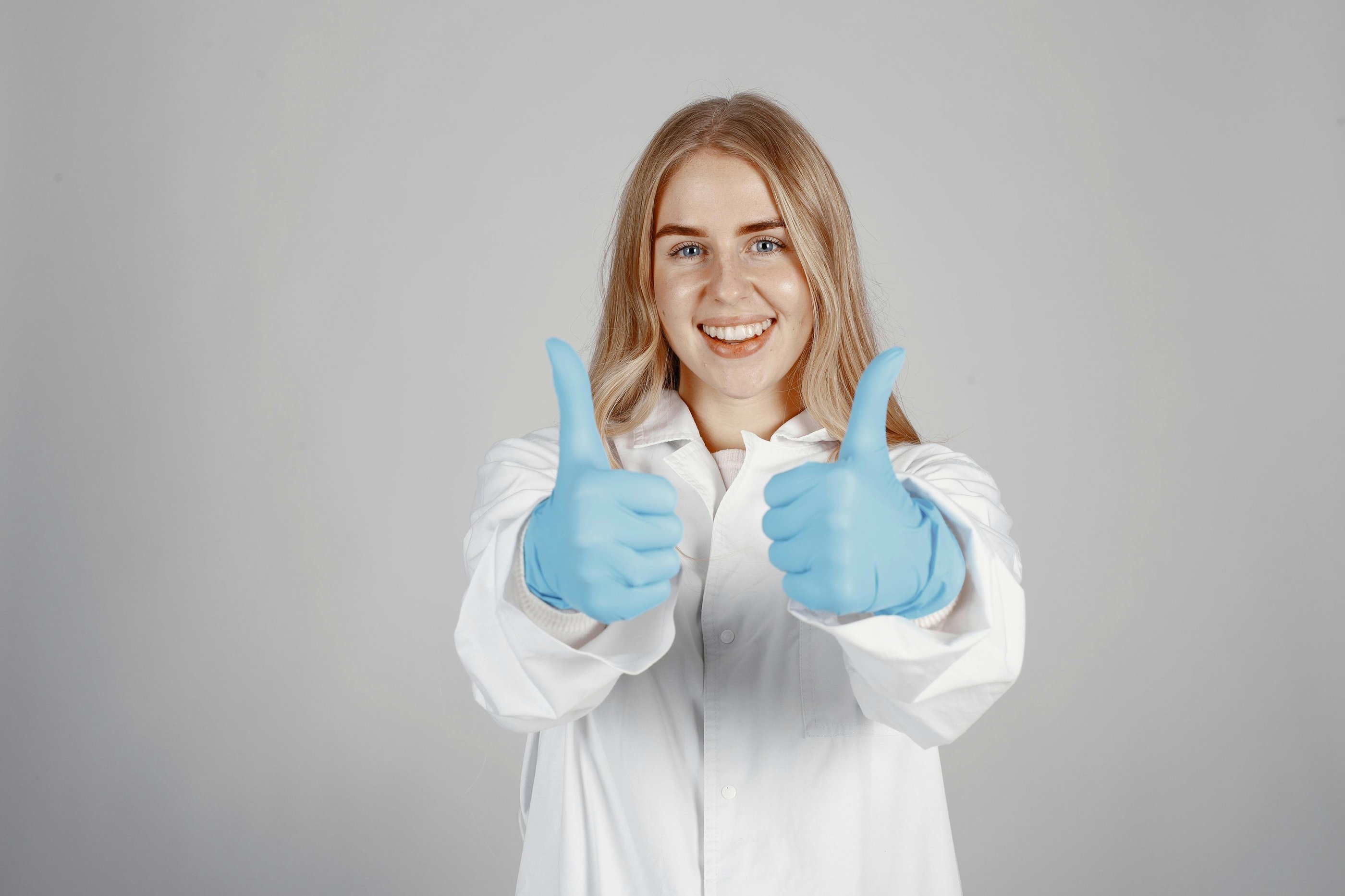 Female in lab coat with blue gloves giving thumbs up sign