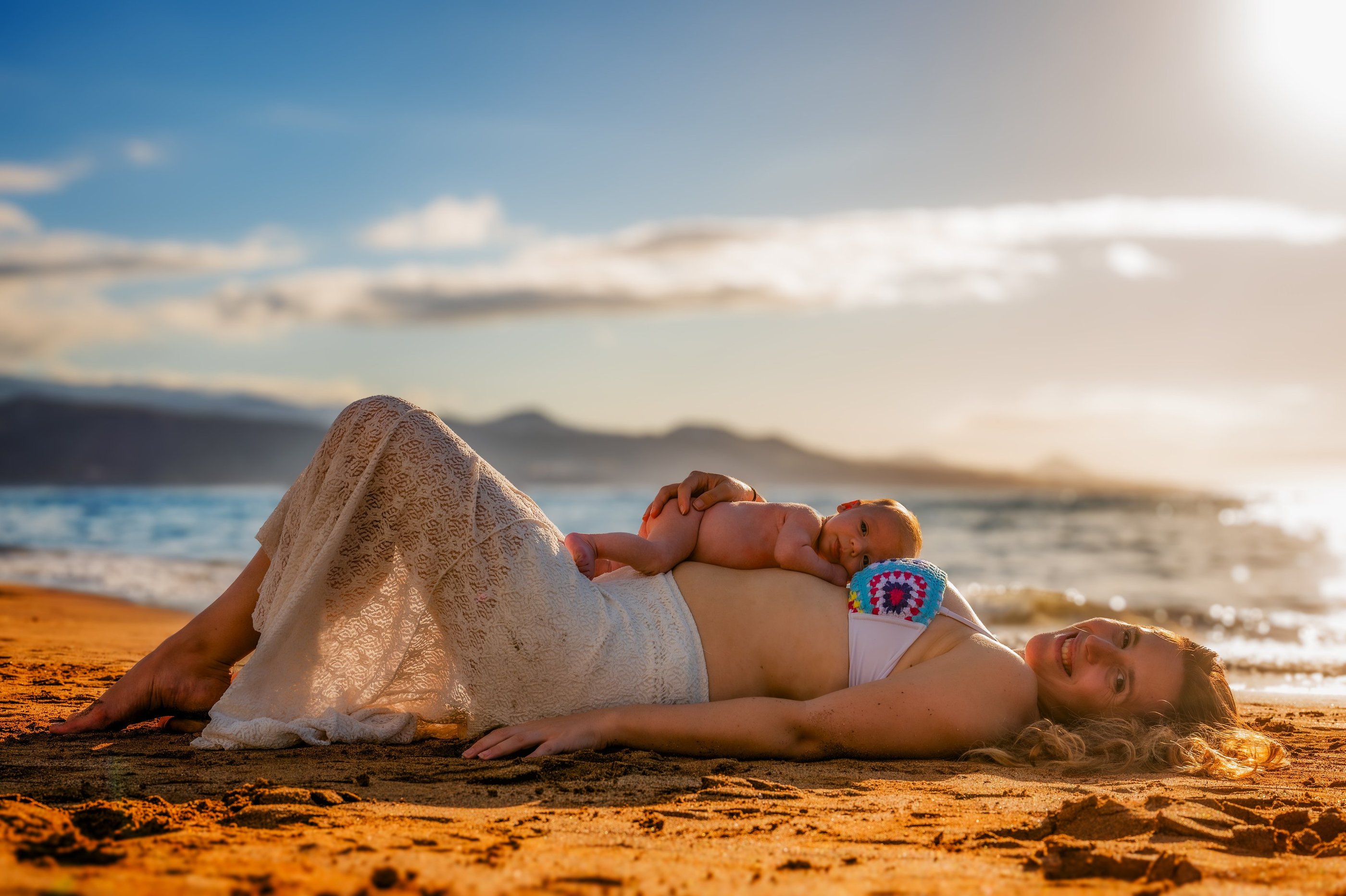 a pregnant woman laying on a beach