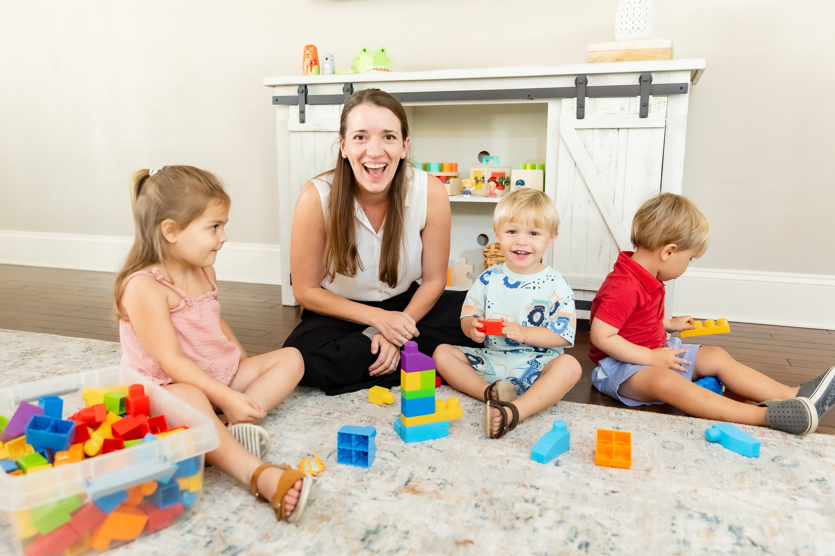 Therapist and a group of young children smiling at the camera, playing with blocks 