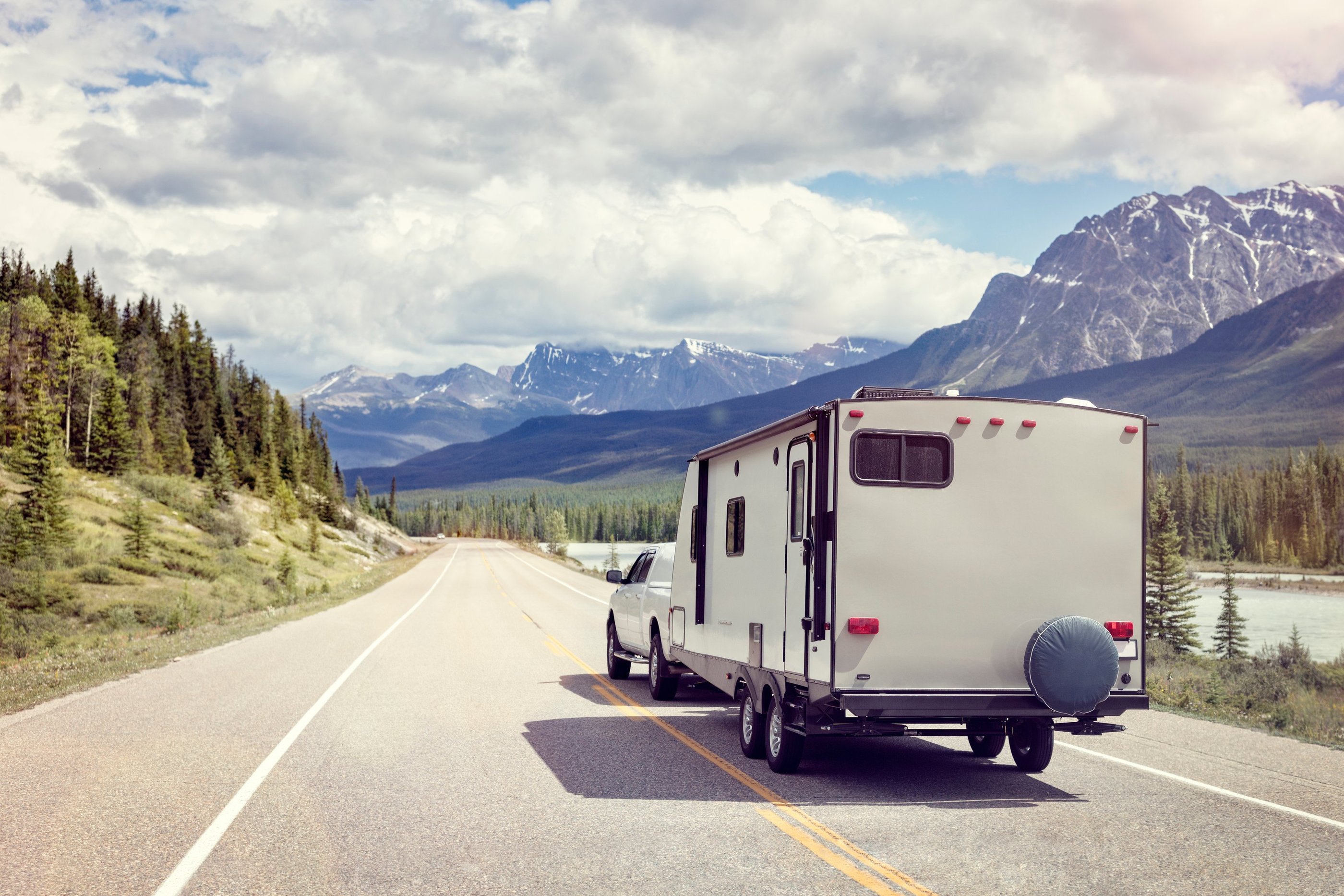 RV driving down road with mountains and trees.