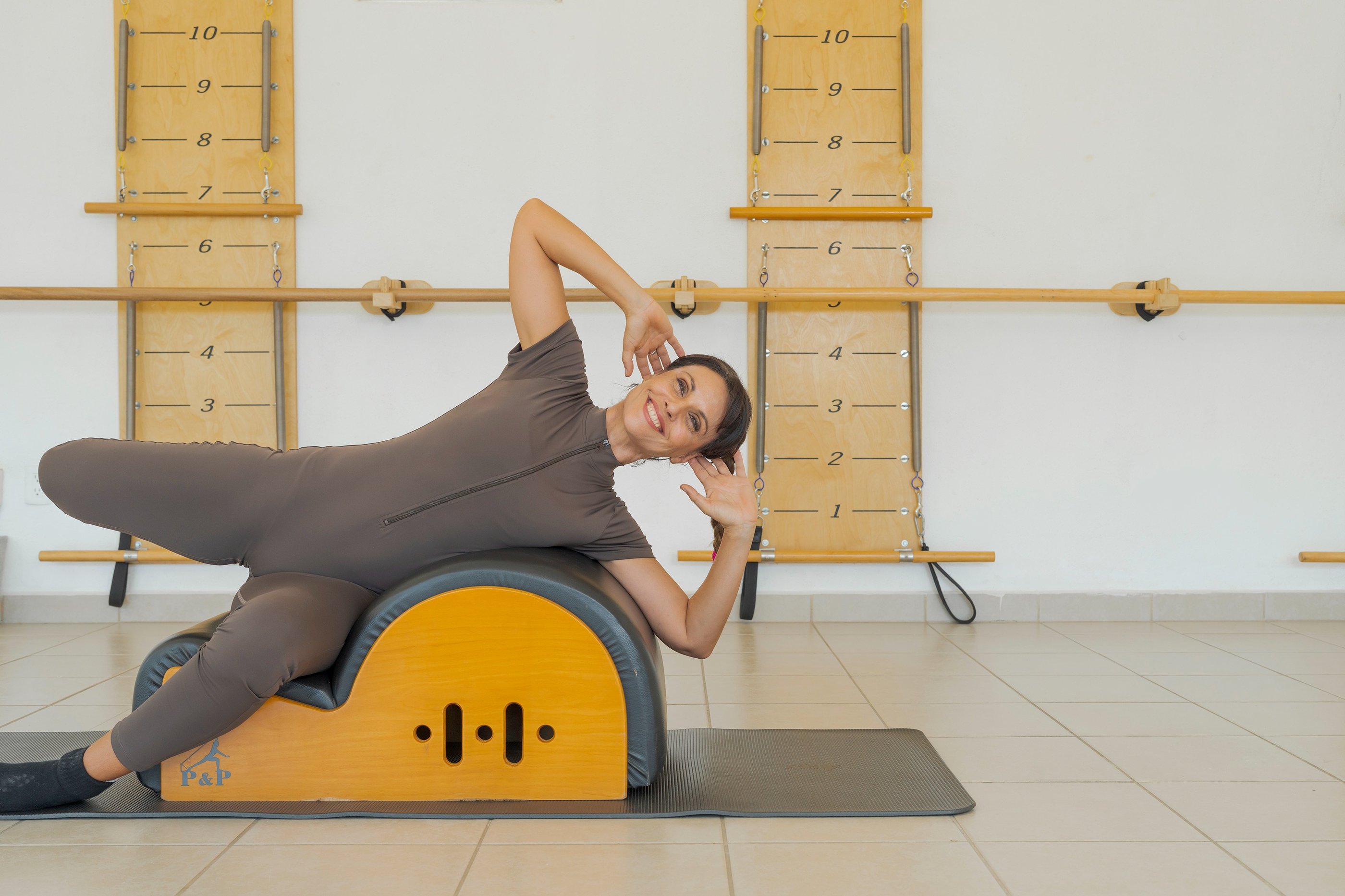 Woman smiling while performing a side bend exercise on a Pilates Spine Corrector barrel.