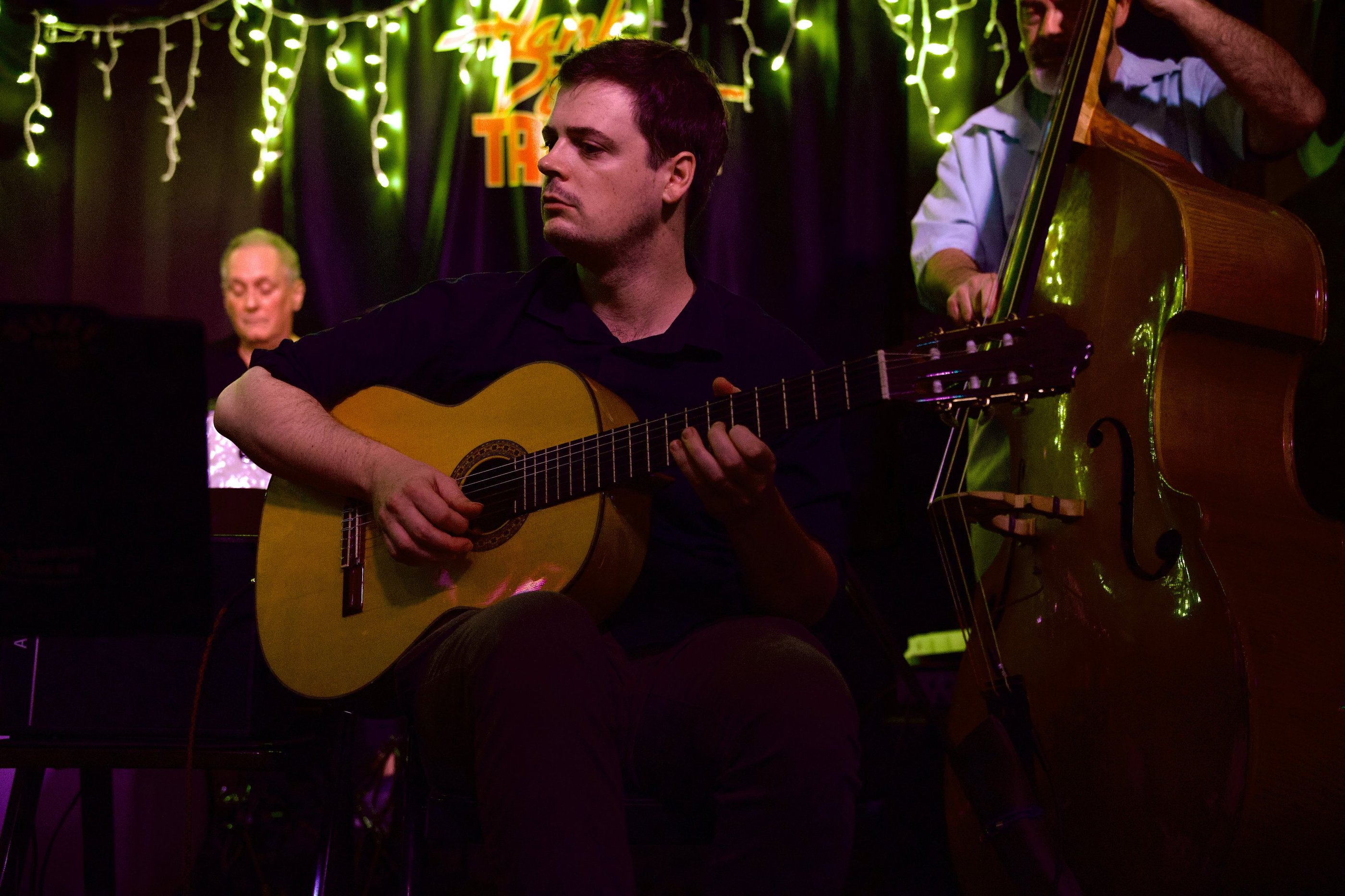 a man (rob coleman) playing acoustic guitar with a drummer and bassist