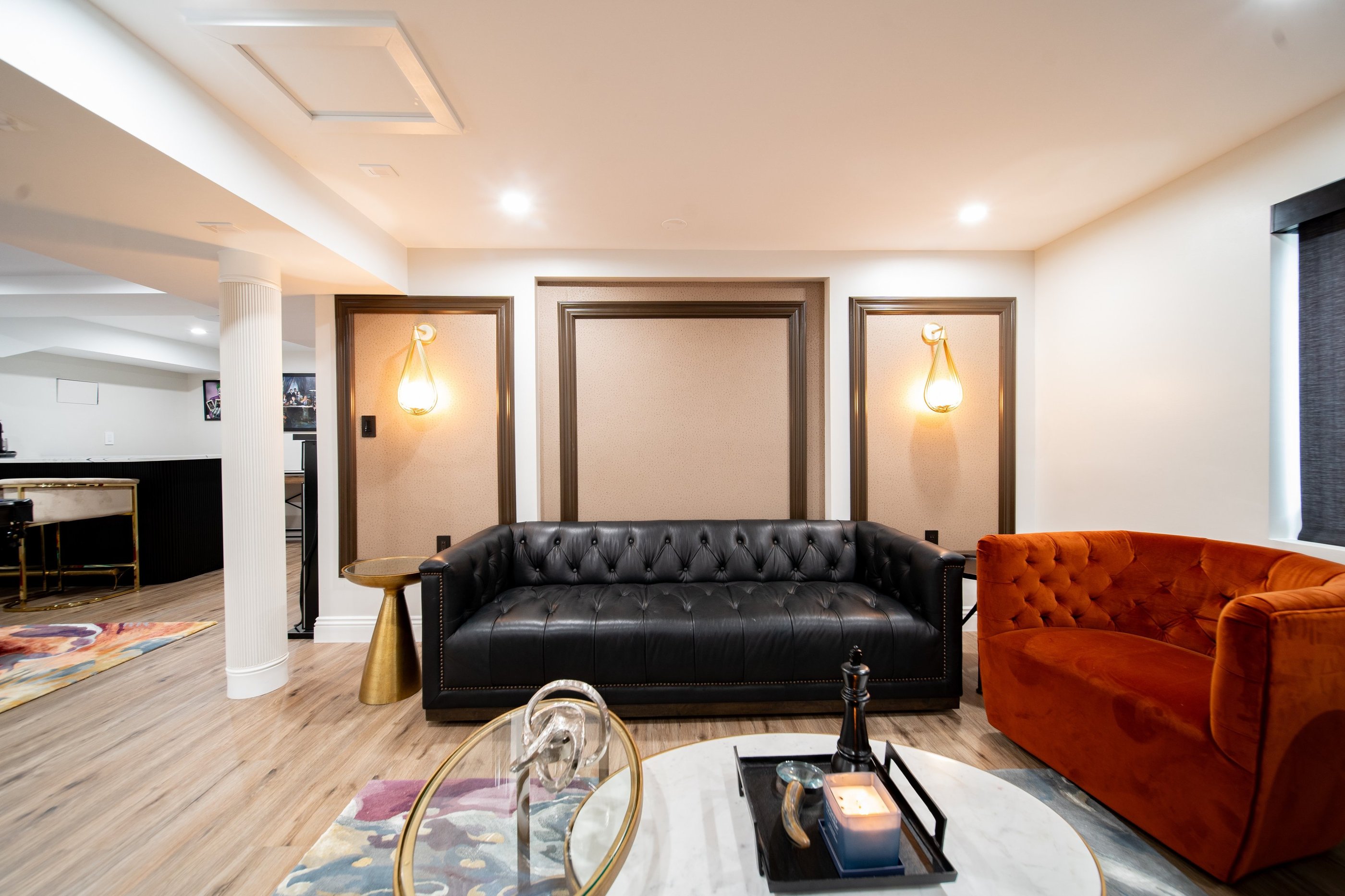 Modern luxury lounge featuring a black tufted leather sofa and orange velvet armchair with elegant wall sconces.