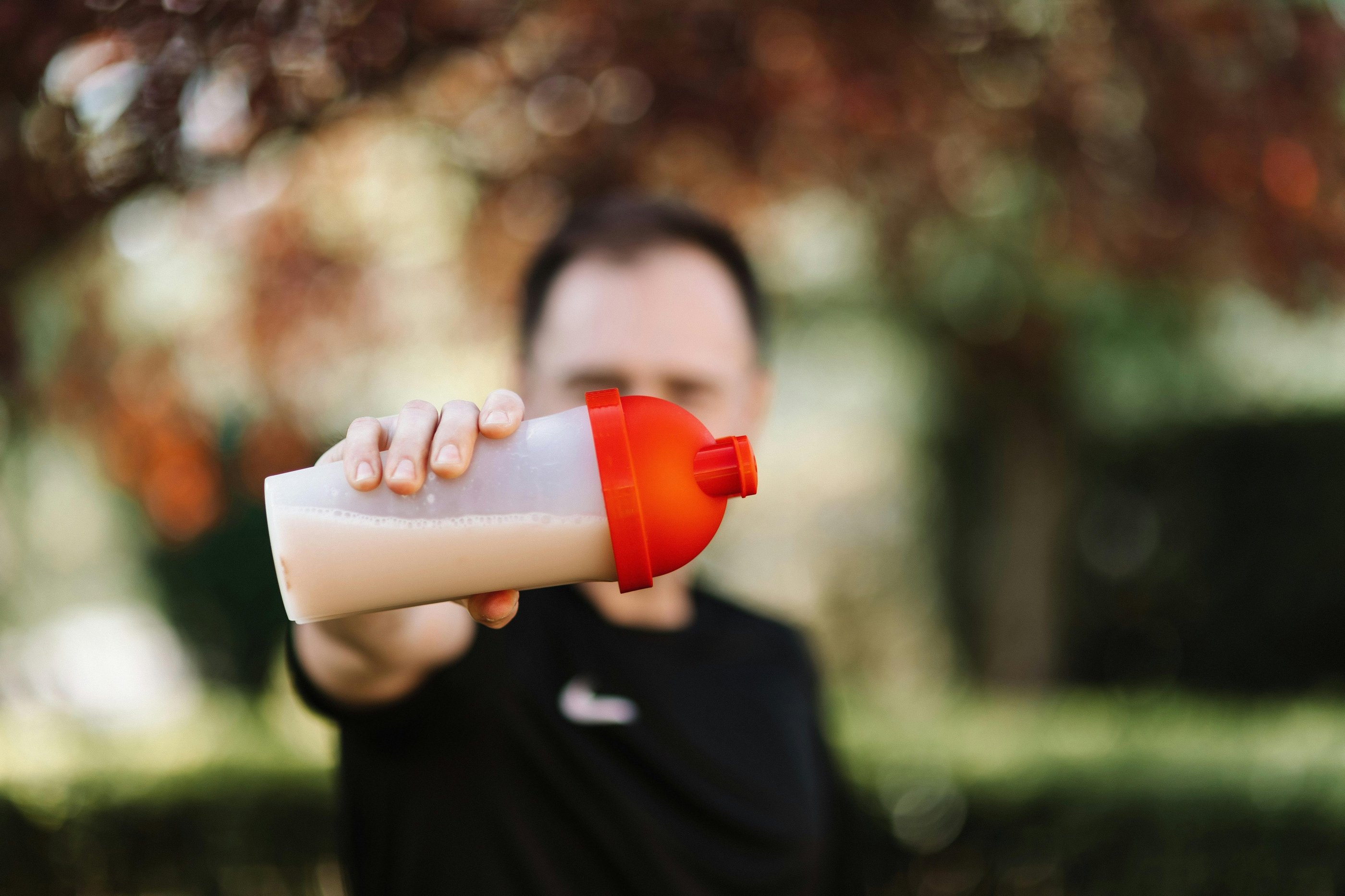A man holding a protein shaker bottle with a red lid after an outdoor workout session.