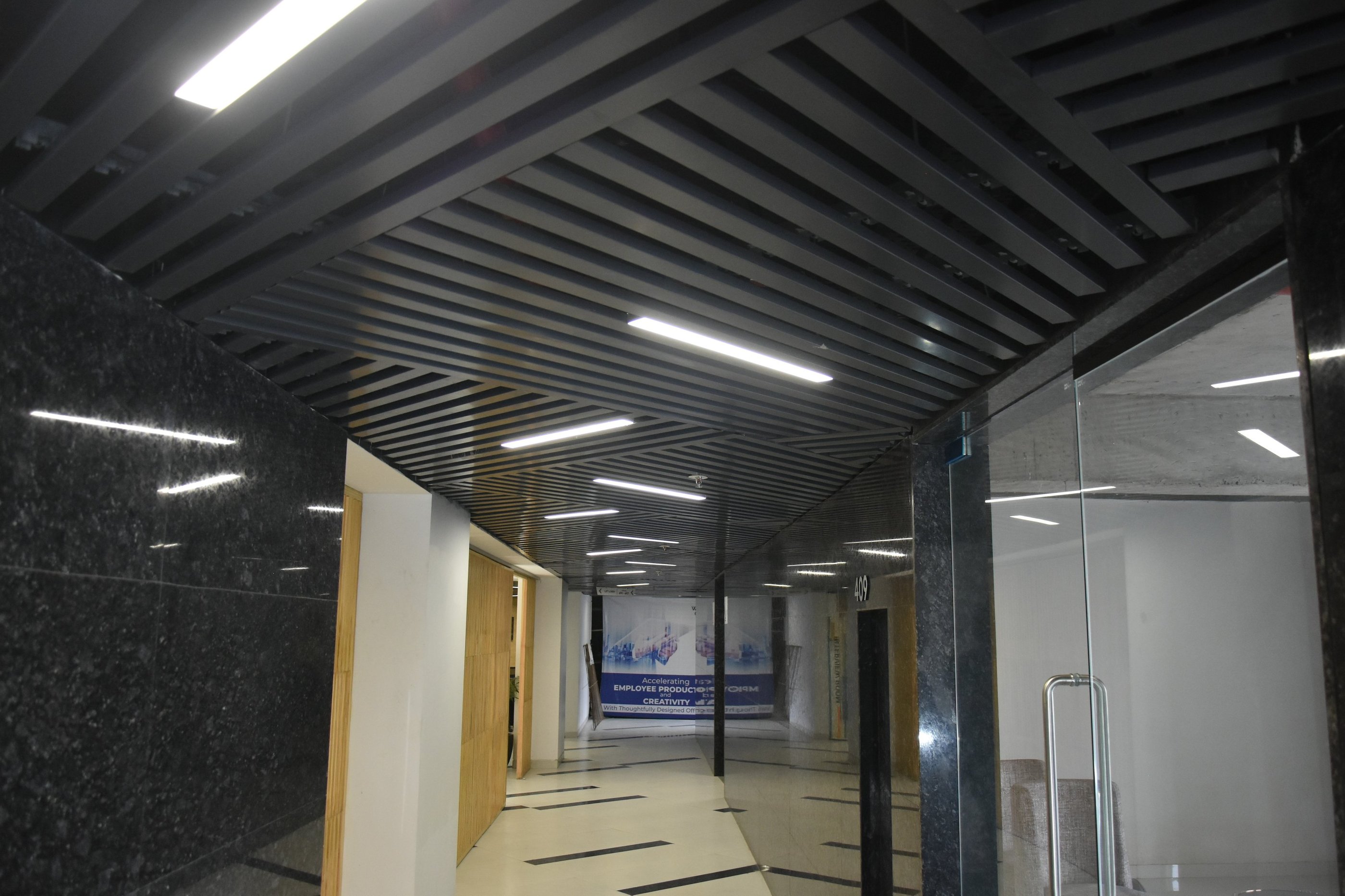 Modern office hallway with dark louvered ceiling, bright LED lights, and marble walls.