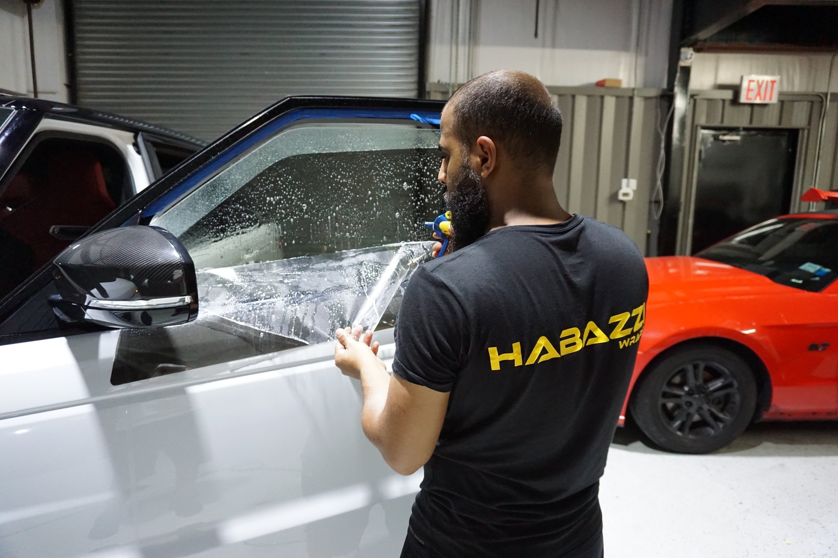 Professional auto technician applying tints film to a white SUV window for UV protection.