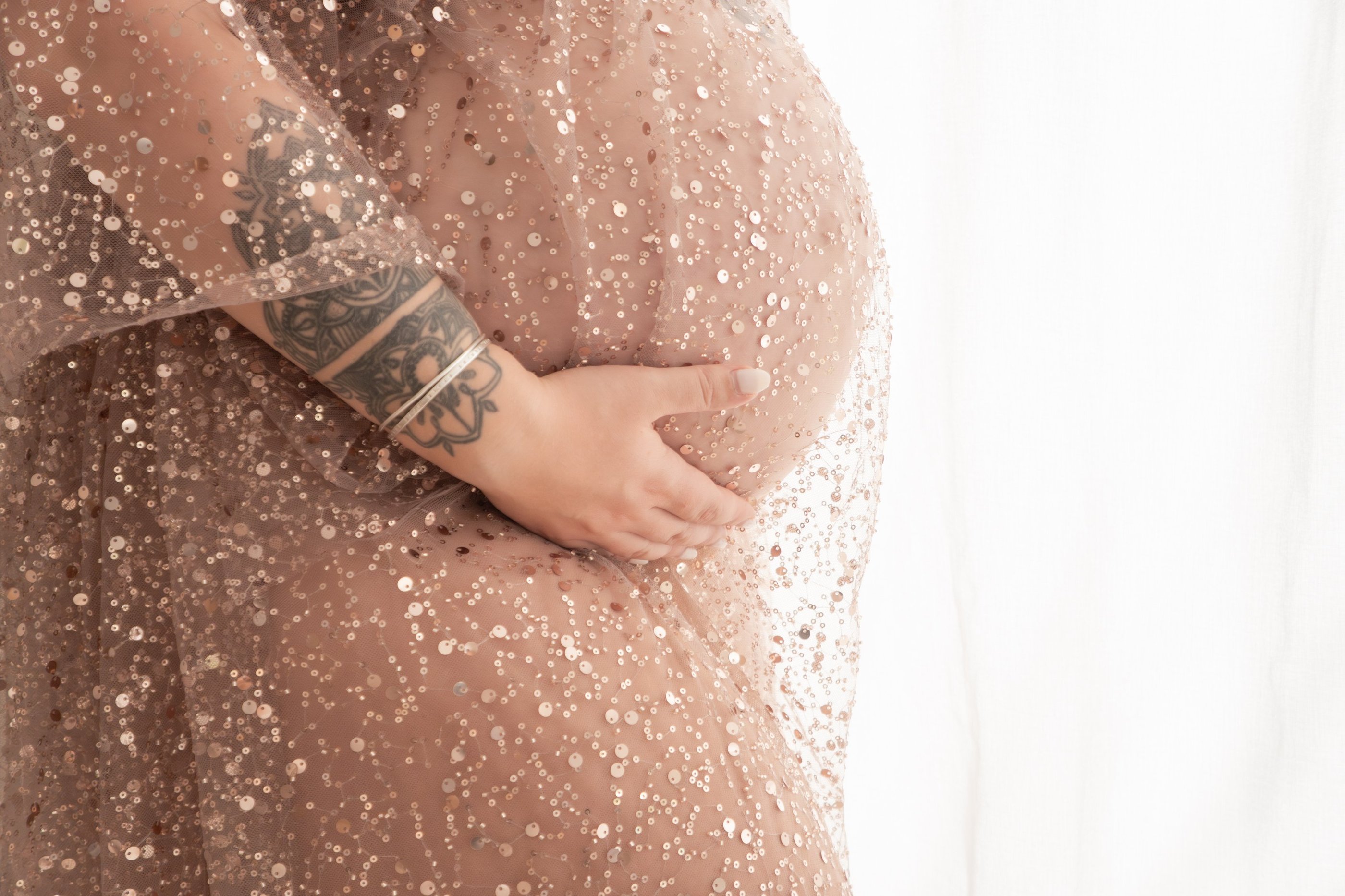 Maternity photoshoot featuring a pregnant woman with tattoos in a rose gold sequin gown.