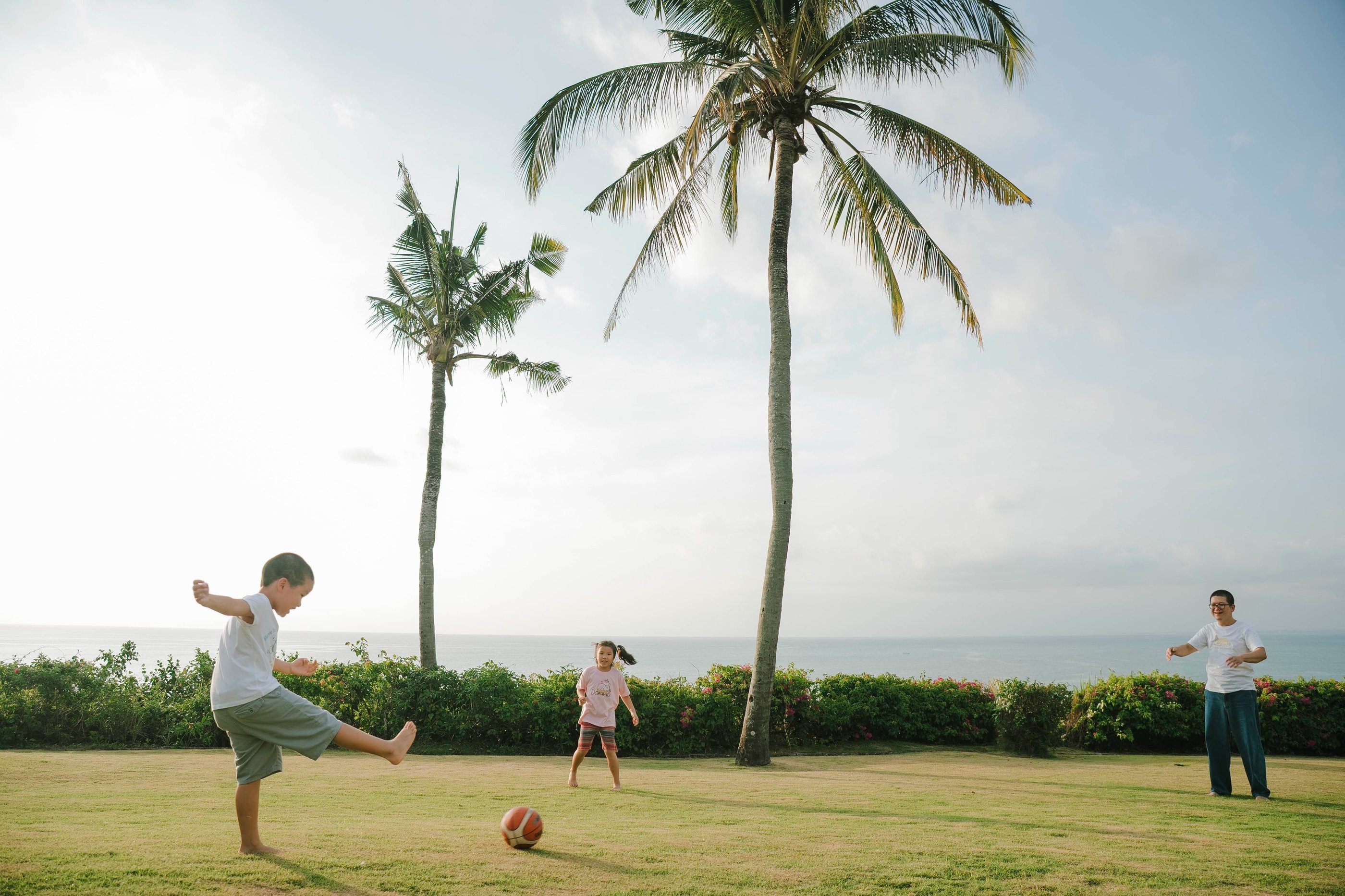 Father and children playing football on the oceanfront lawn at AYANA Villas Jimbaran Bali