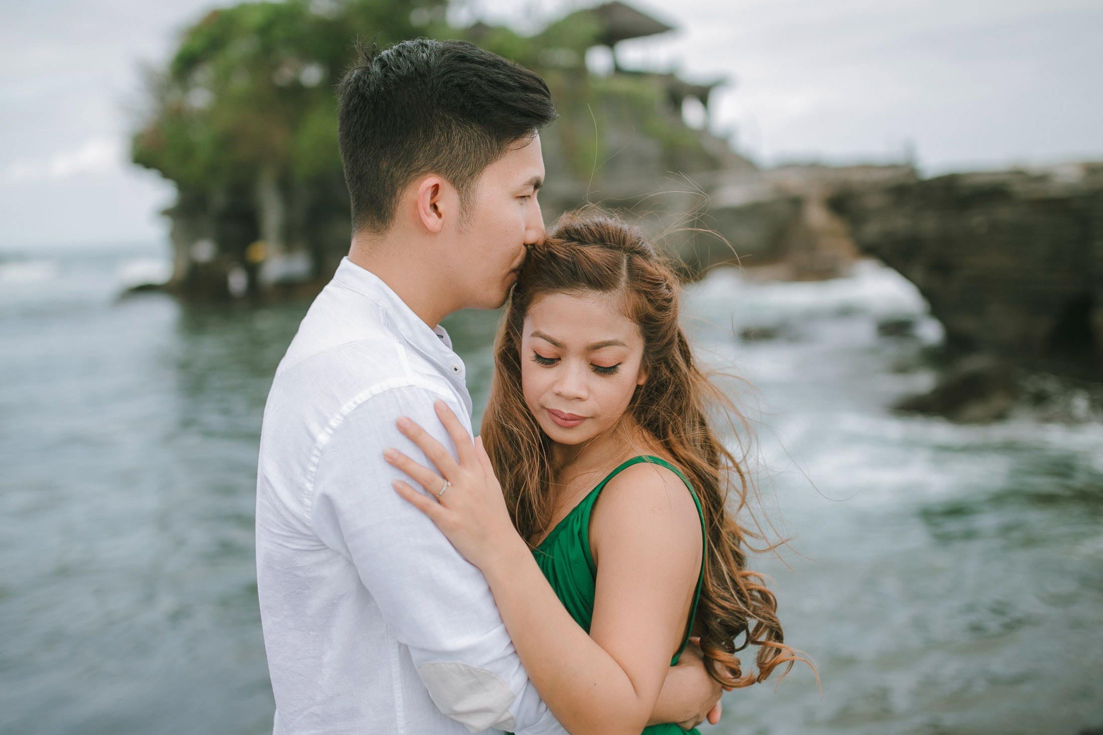 Intimate couple embrace with ocean backdrop at Tanah Lot Bali.