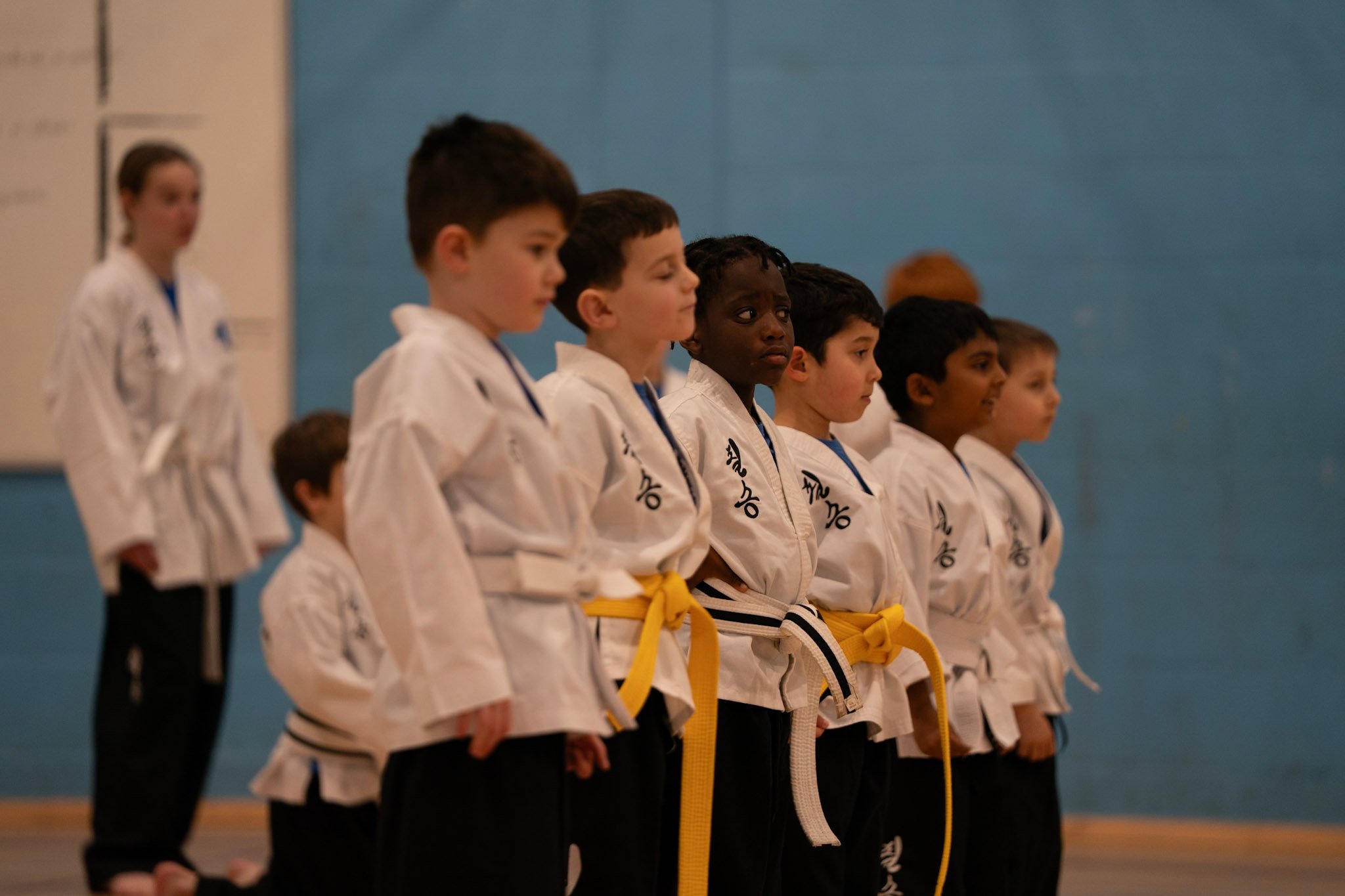 Diverse group of children wearing white uniforms in a karate class lineup for martial arts training.
