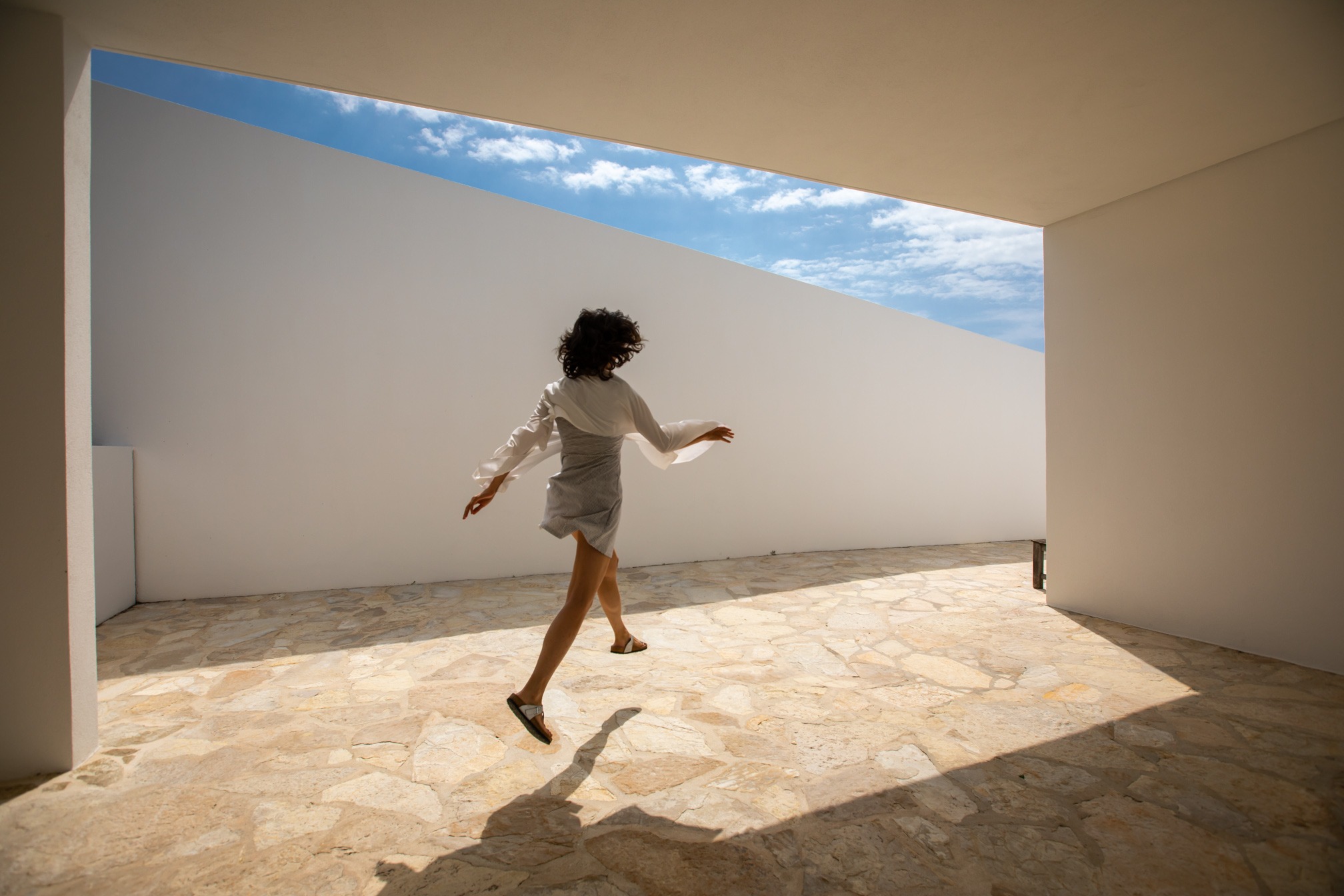 a woman in a white shirt and skirt jumping on a tiled floor in an architect house