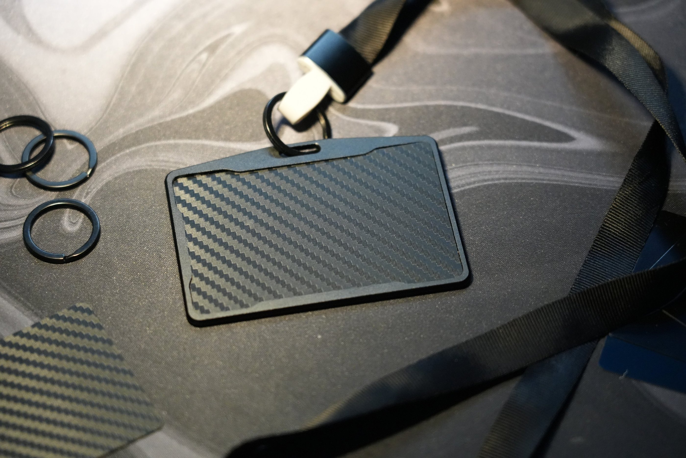 Black carbon fiber ID badge holder with a neck lanyard and key rings on a desk.