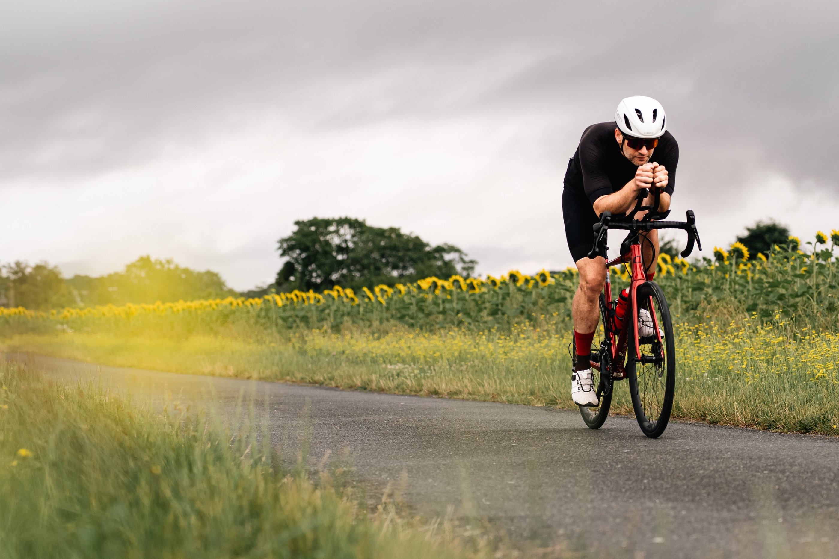Cycliste en plein effort sur une route de campagne, bouton d’or flou au premier plan, photographie d