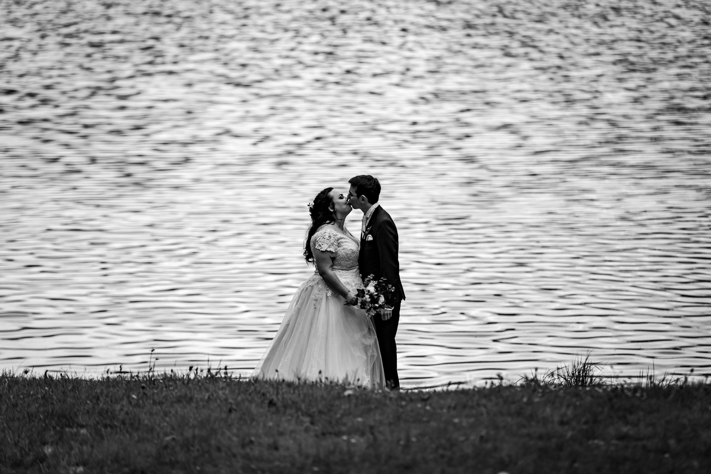 a bride and groom kissing in front of a lake