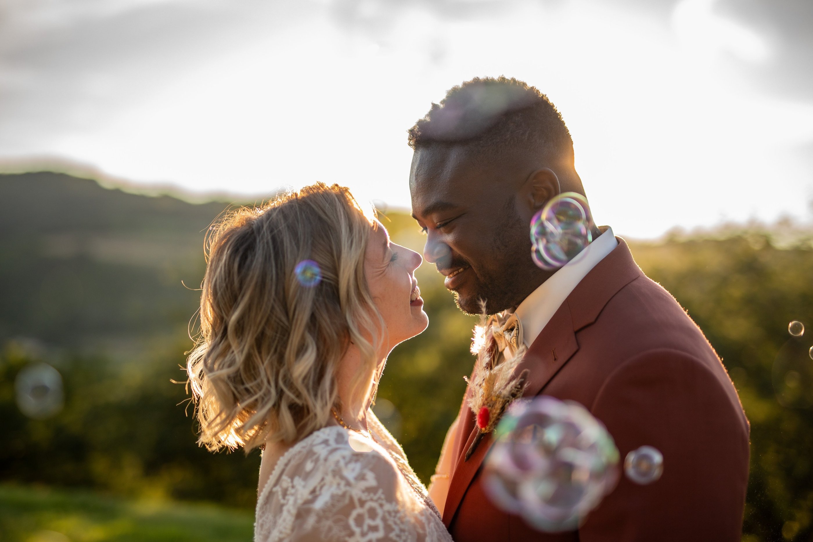 a bride and groom in front of blowing bubbles in the air, in front of the sunset