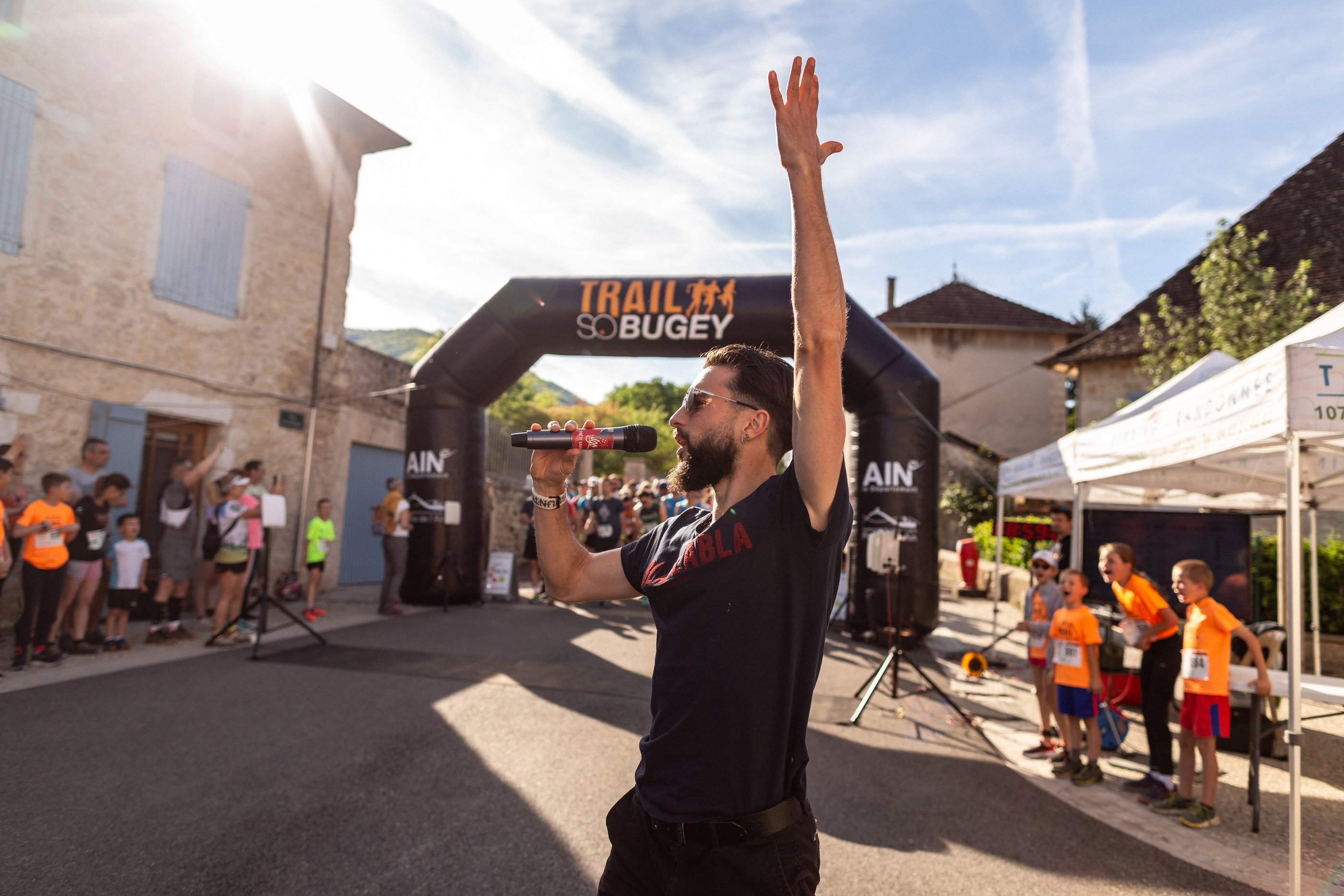 a man in a black shirt speaking with a microphone in a sport event, in front of the starting line