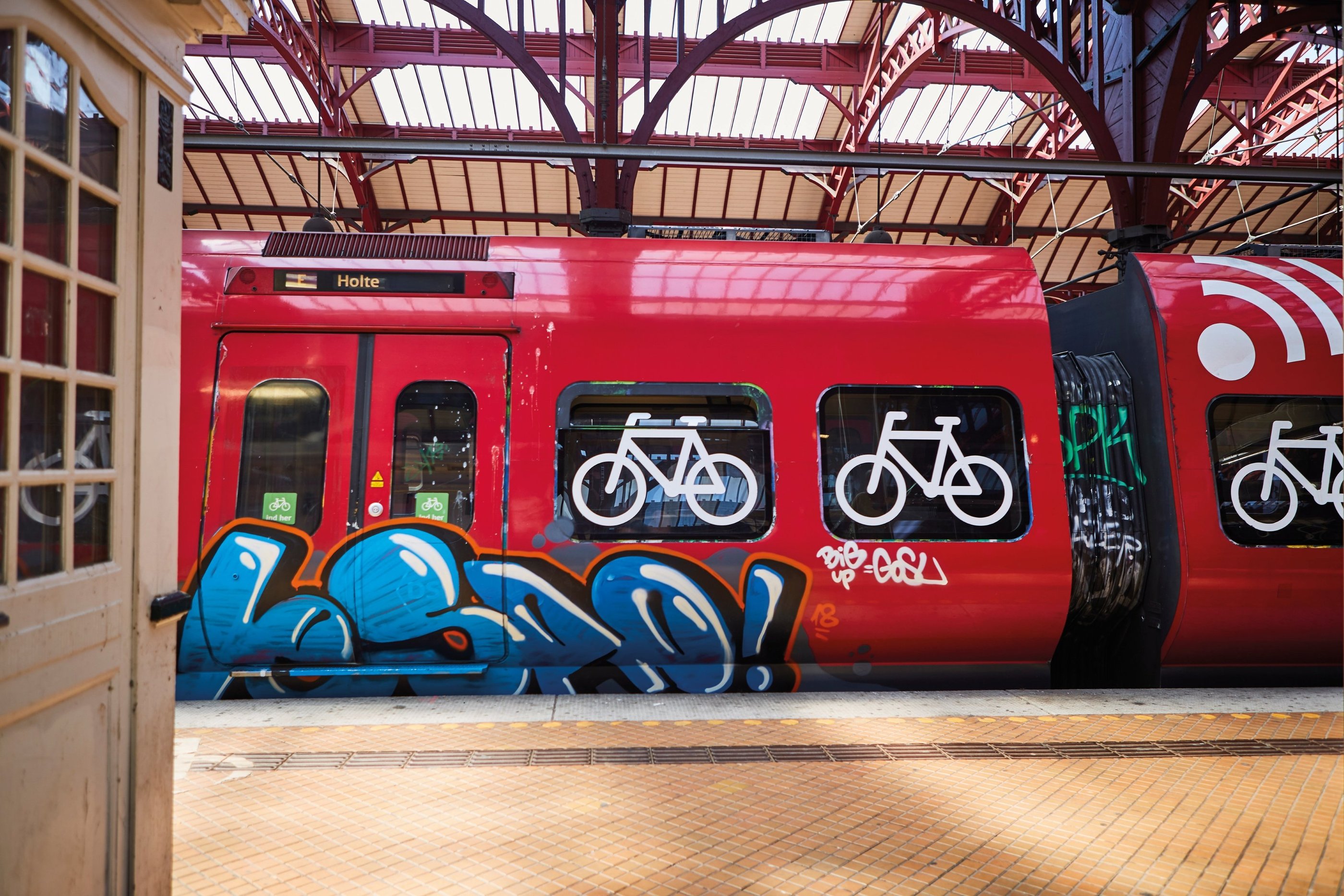 red train with symbols of bicylces at a train station with grafitti on it