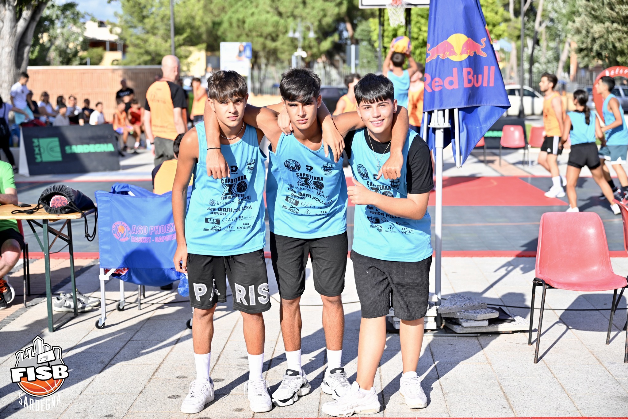 Three young basketball players in light blue jerseys pose at an outdoor 3x3 tournament.
