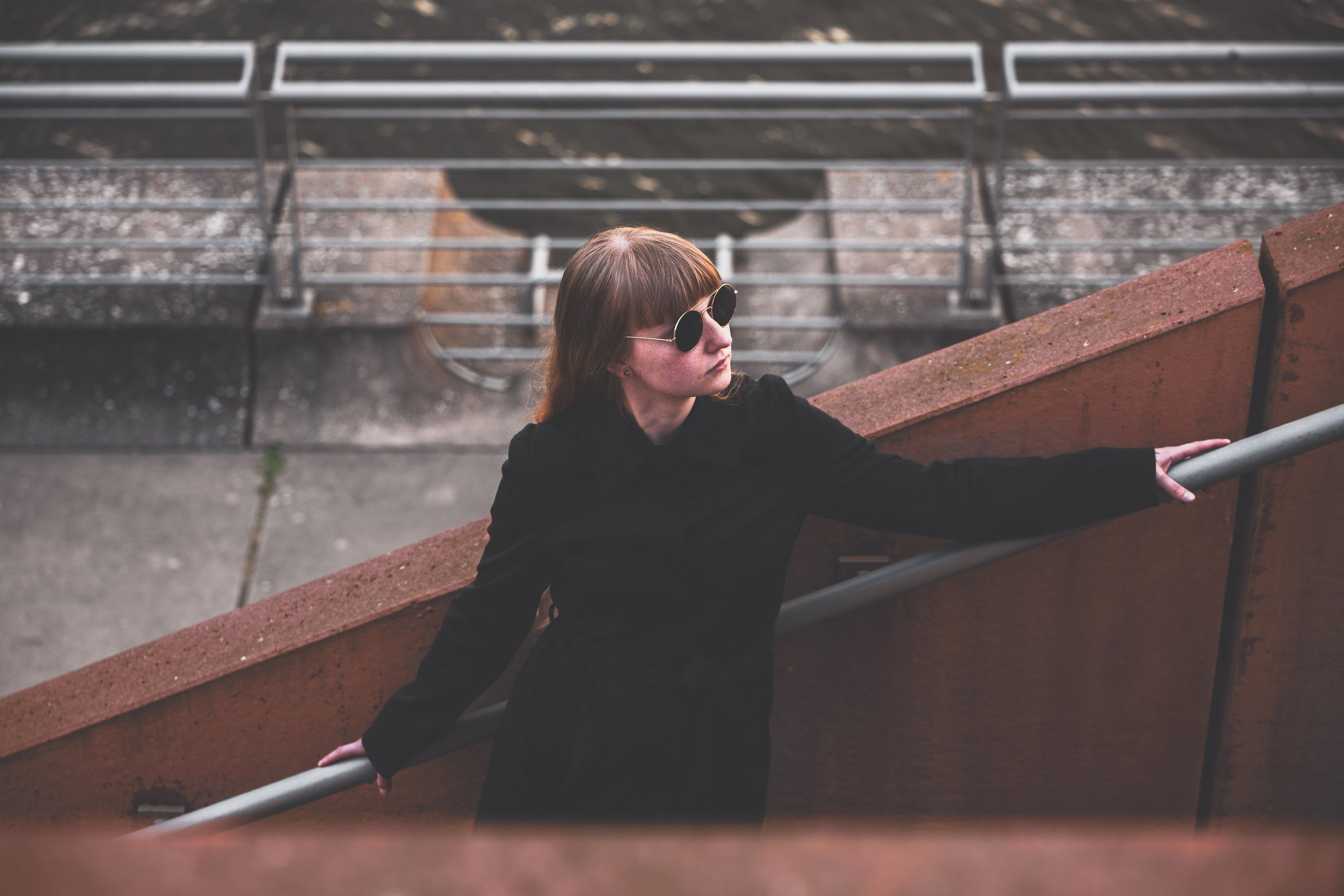 a woman in sunglasses and a black jacket standing on a stair case