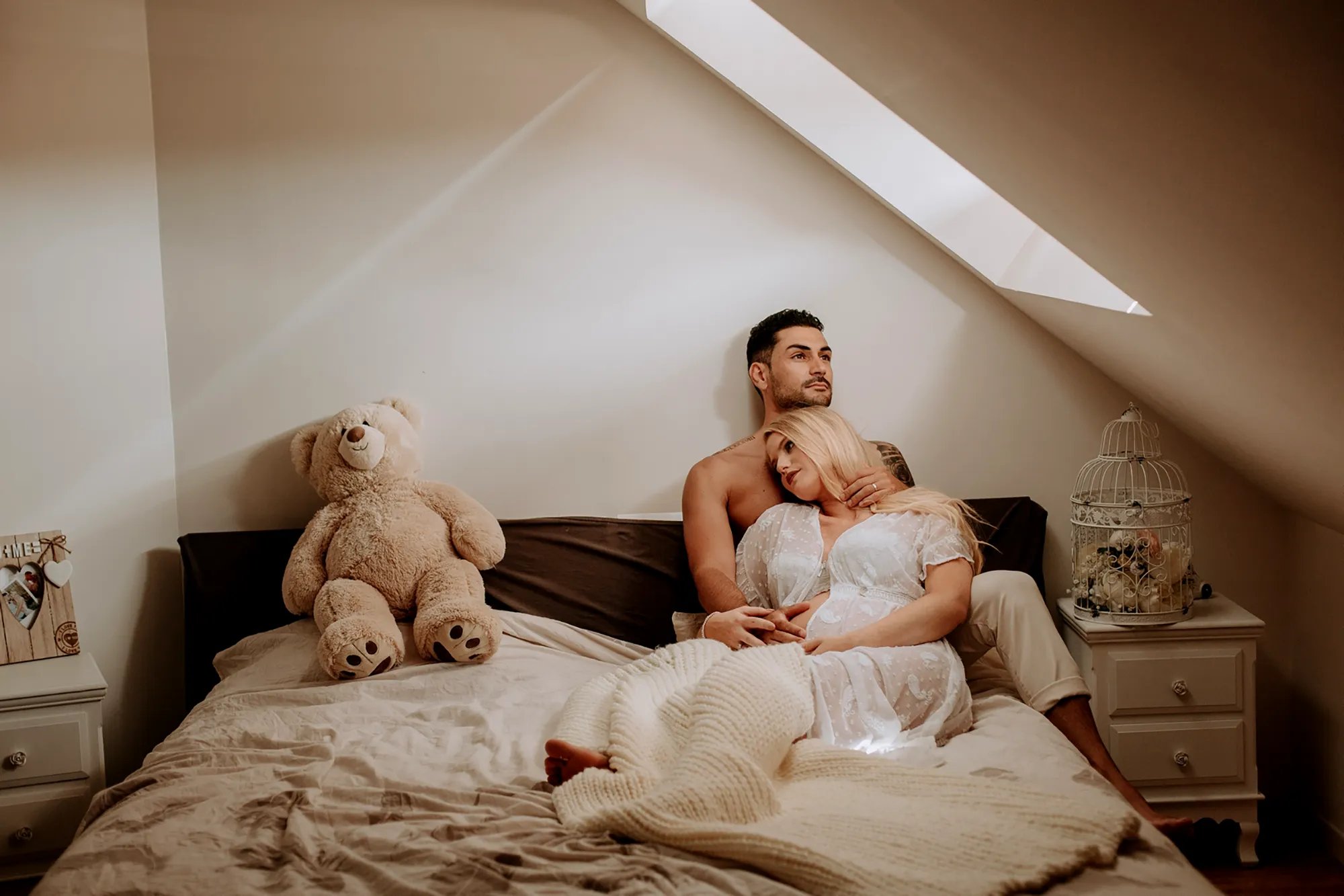 une femme enceinte pose dans son lit avec son conjoint pour une séance photo grossesse