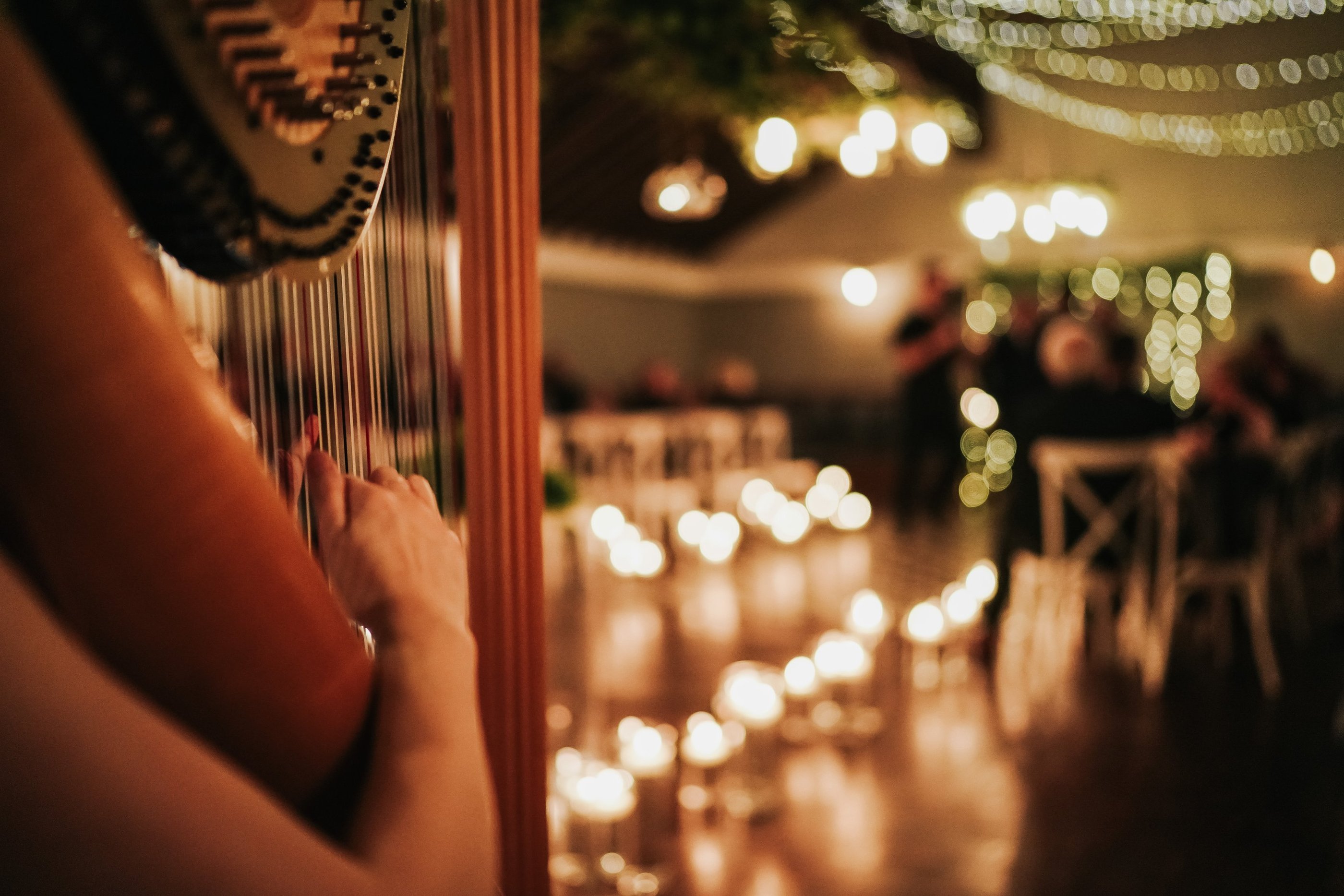 Wedding ceremony with room lit by numerous candles. Harp being performed is focus of the picture.