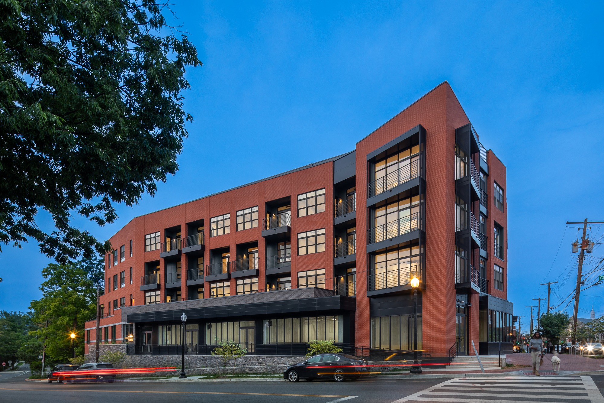 Modern red brick multi-story apartment building with black metal balconies at dusk. 