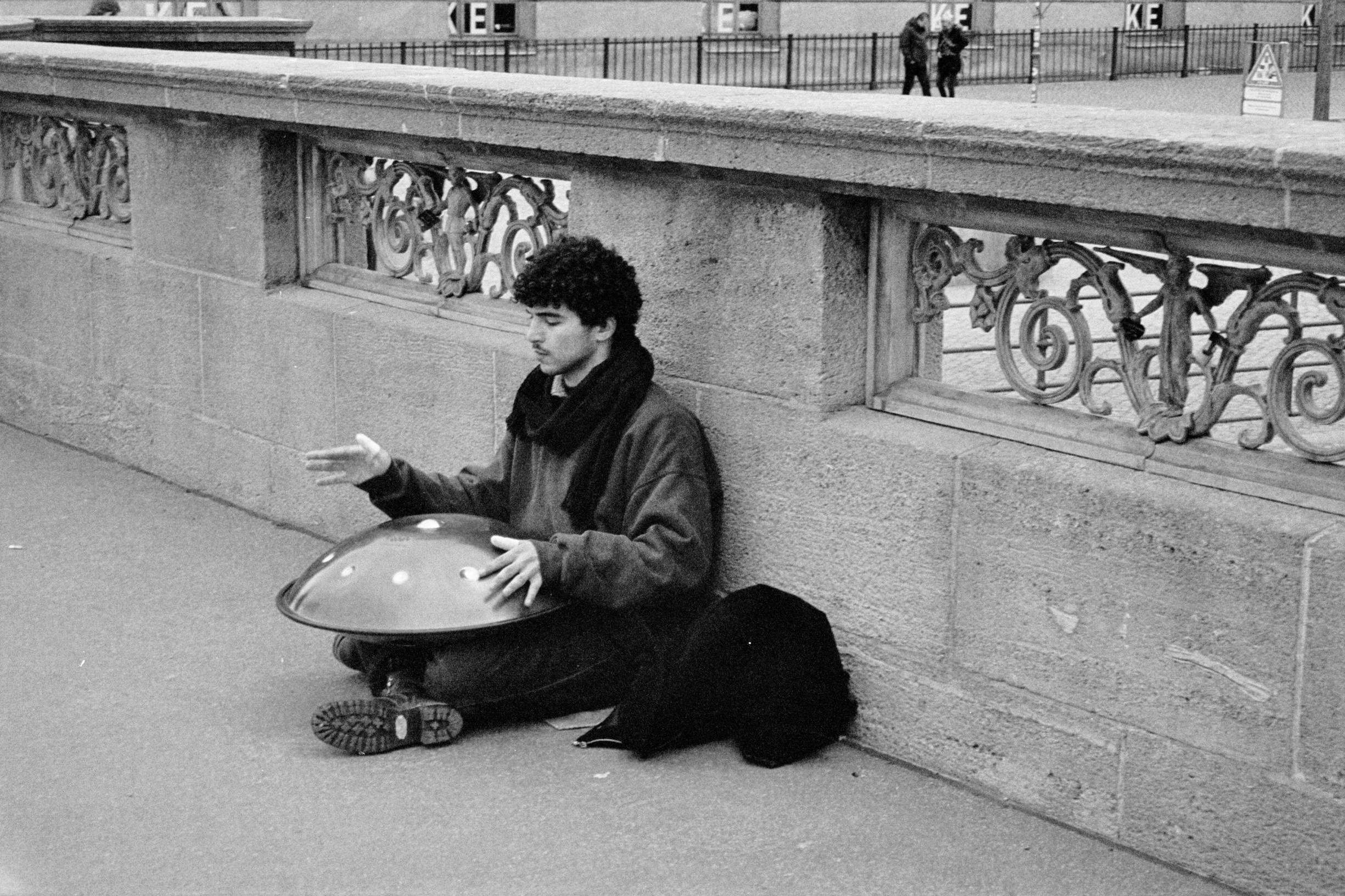 a man sitting on the sidewalk playing the handpan instrument.