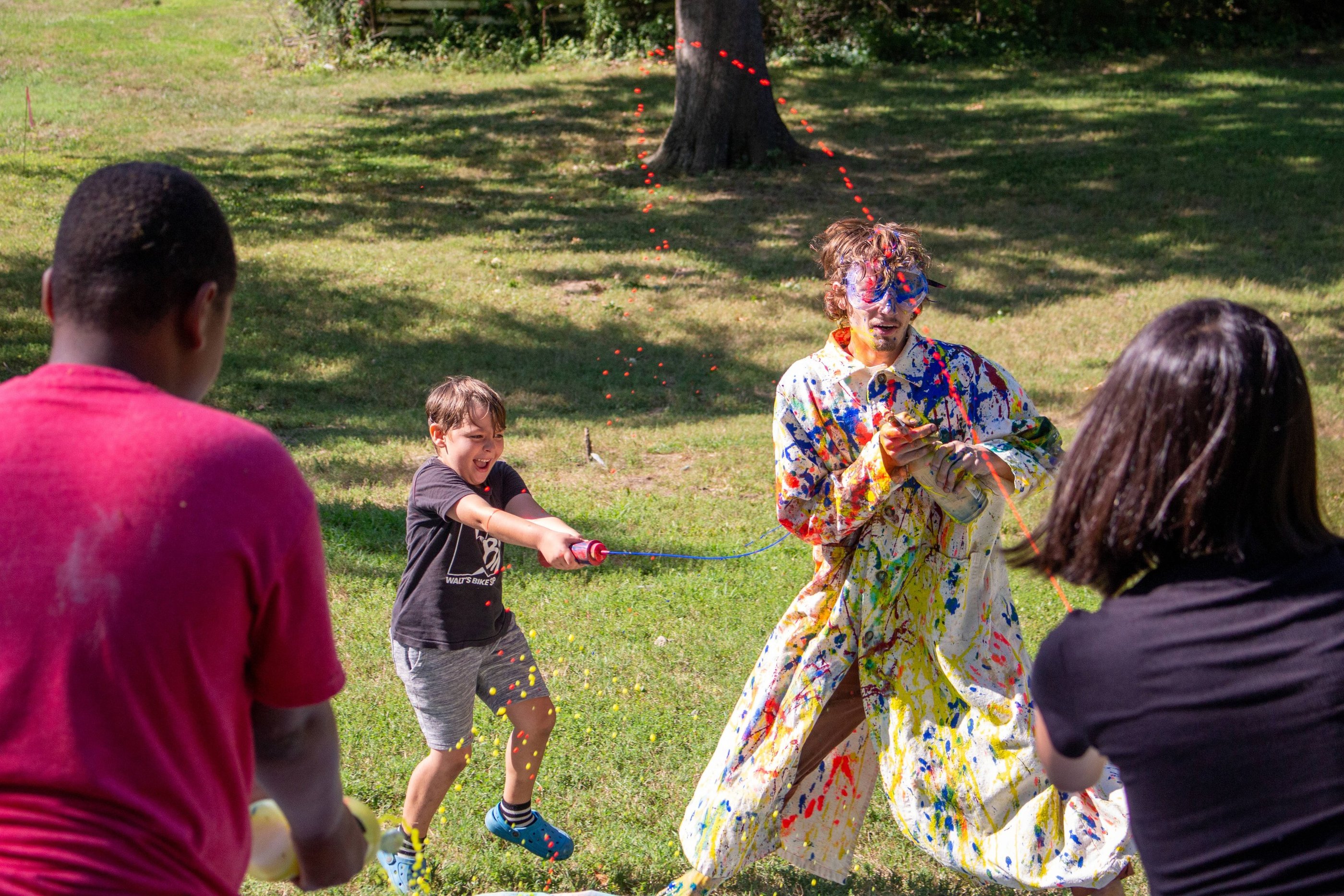 Summer Camp children shooting paint at the teacher in a white trenchcoat.