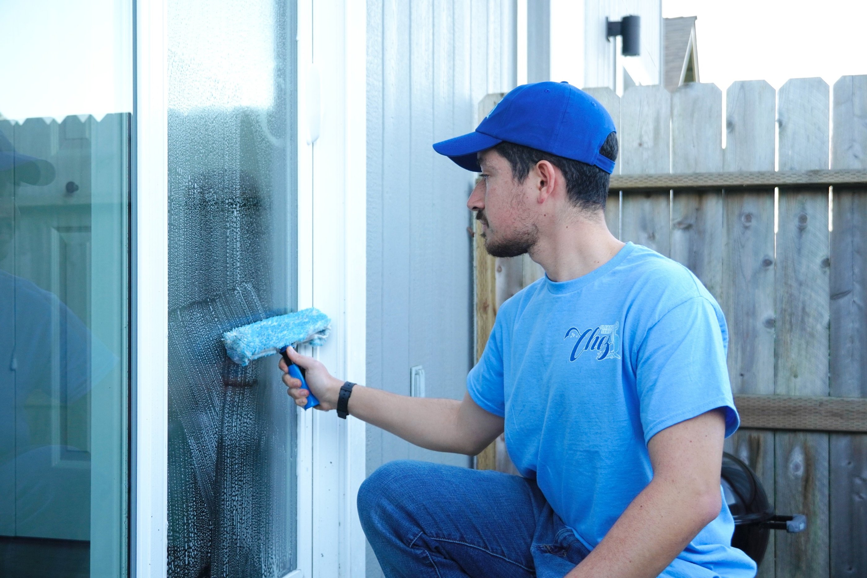 Cleaner from Chez Cleaning Services washing a glass door with a soapy scrubber
