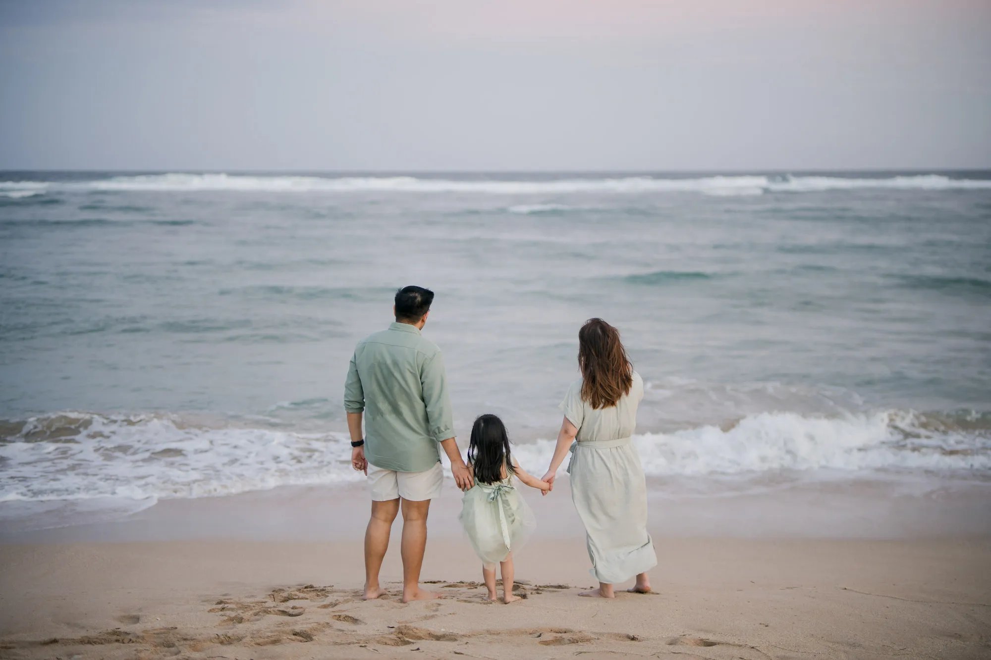 Family standing together facing the ocean during a beach family photography session in Bali.