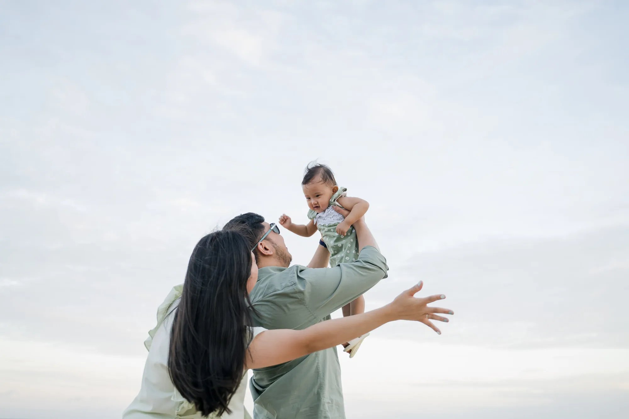 Mother lifting her daughter with the ocean in the background during a family photography session in Bali.
