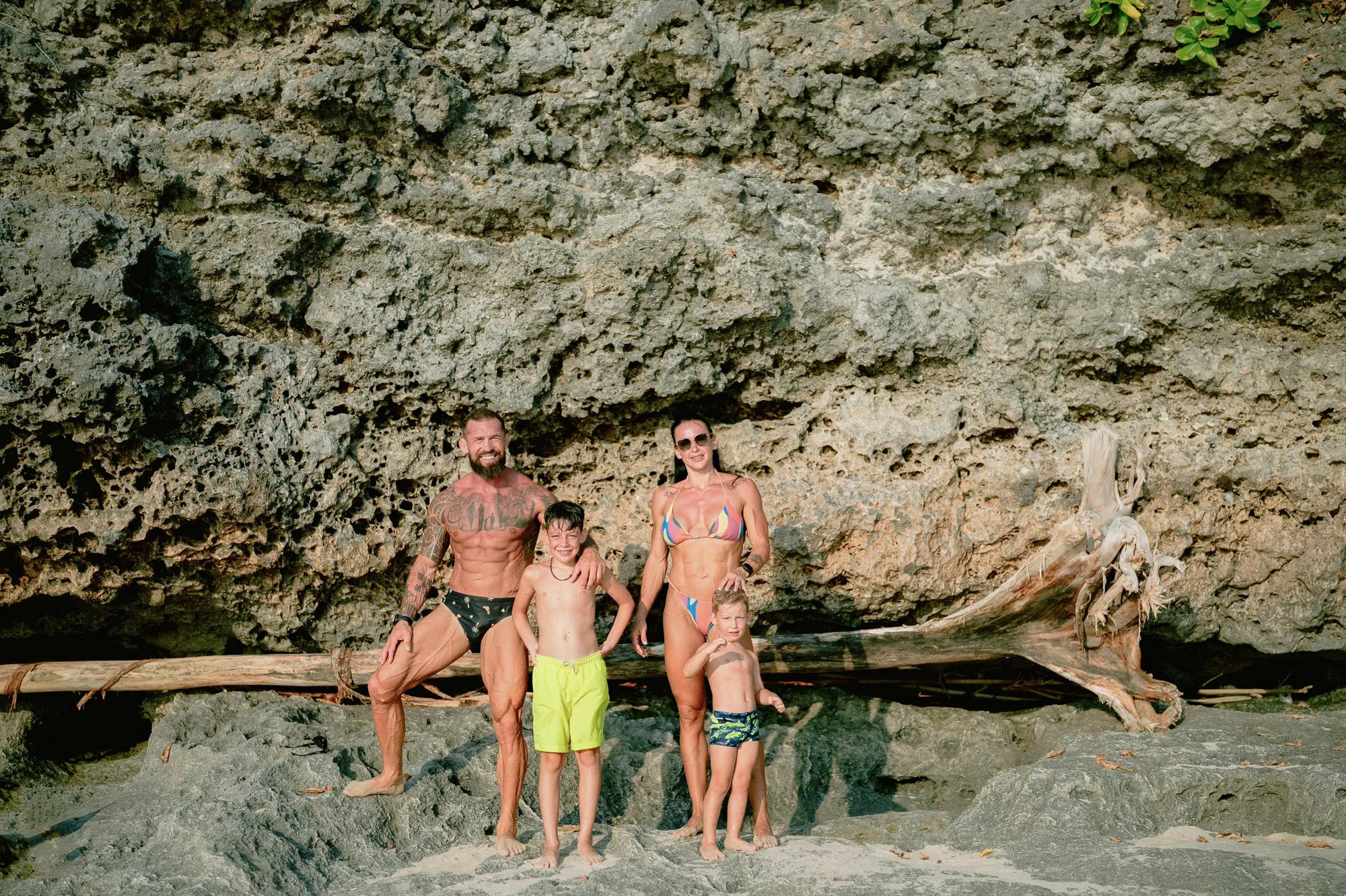 Family standing beneath a coastal cliff during a beach family photography session at Dreamland Beach Bali.