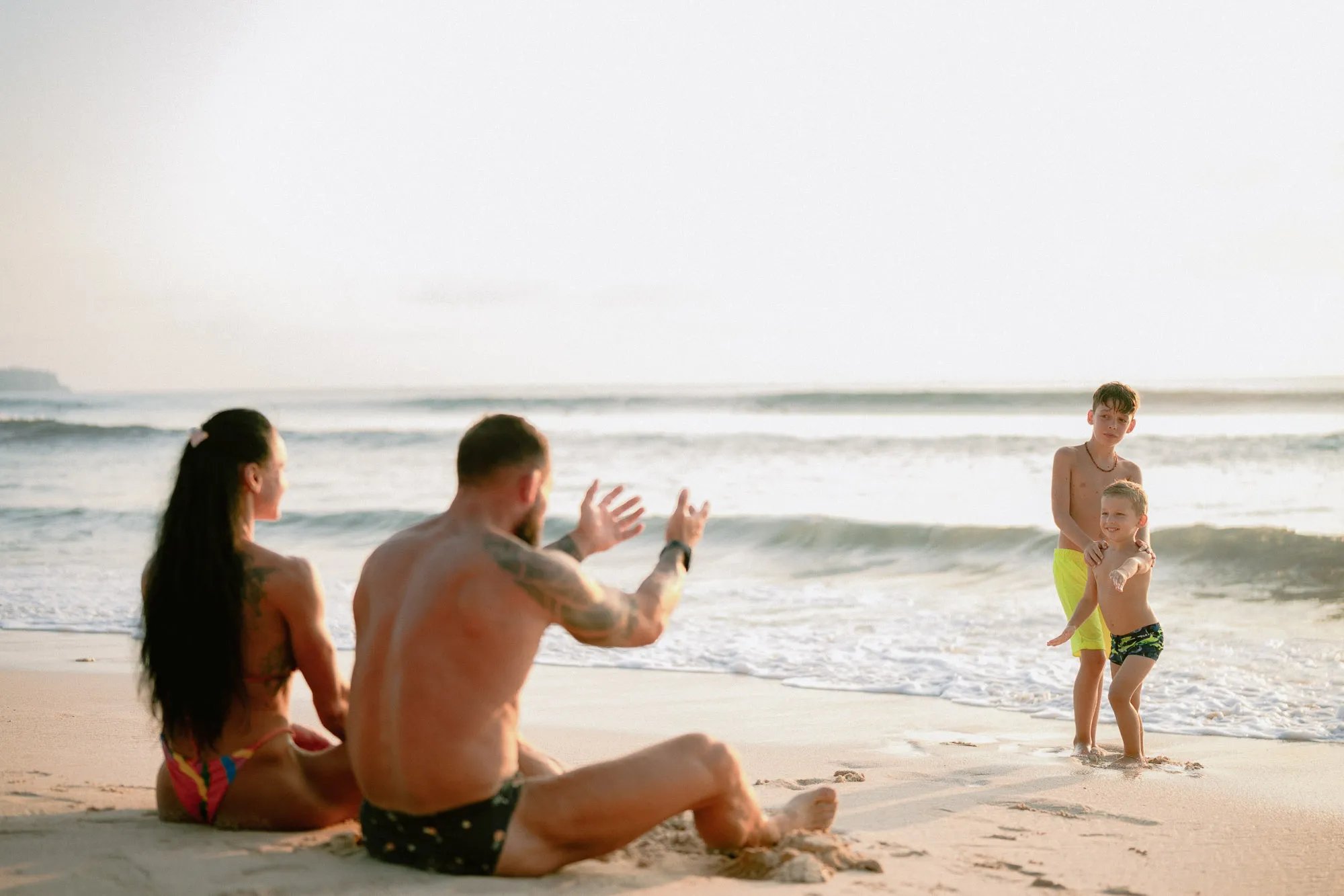 Parents relaxing by the beach while watching their son during a family photography session at Dreamland Beach Bali.
