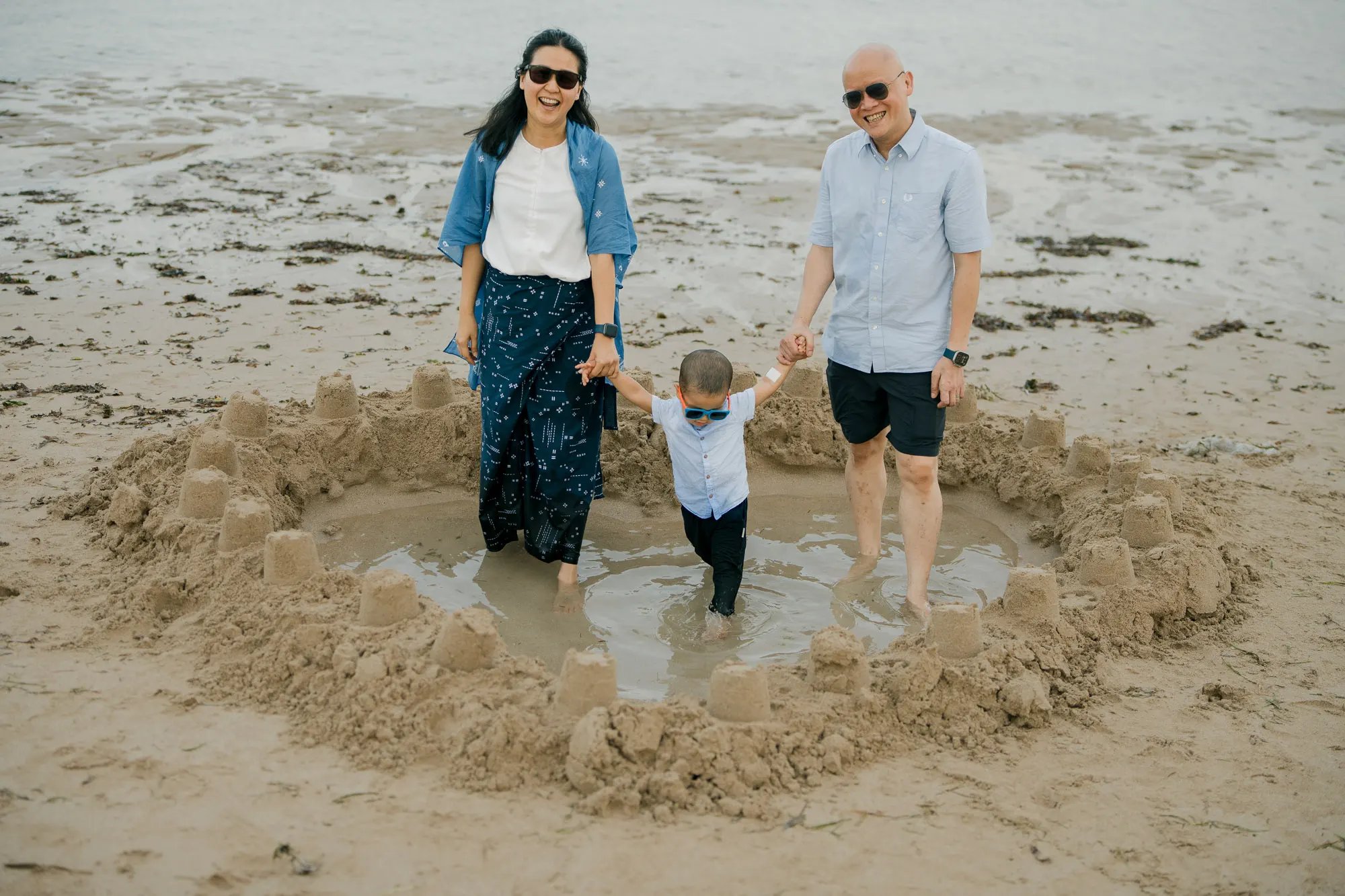 Family walking barefoot across the sand during a natural family photography session at Nusa Dua Beach Bali