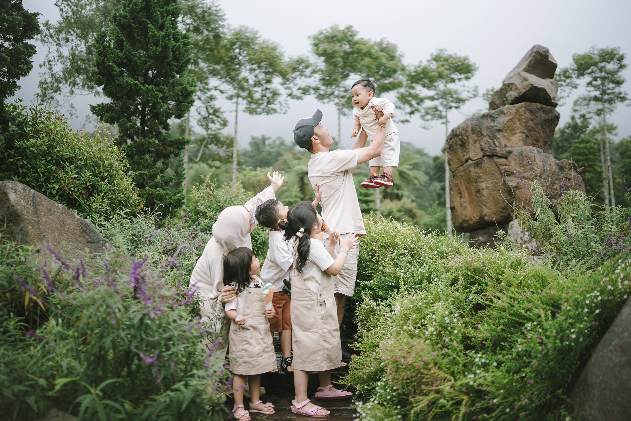 Father lifting child in flower garden during a family photography session at Bali Farm House Bedugul Bali.