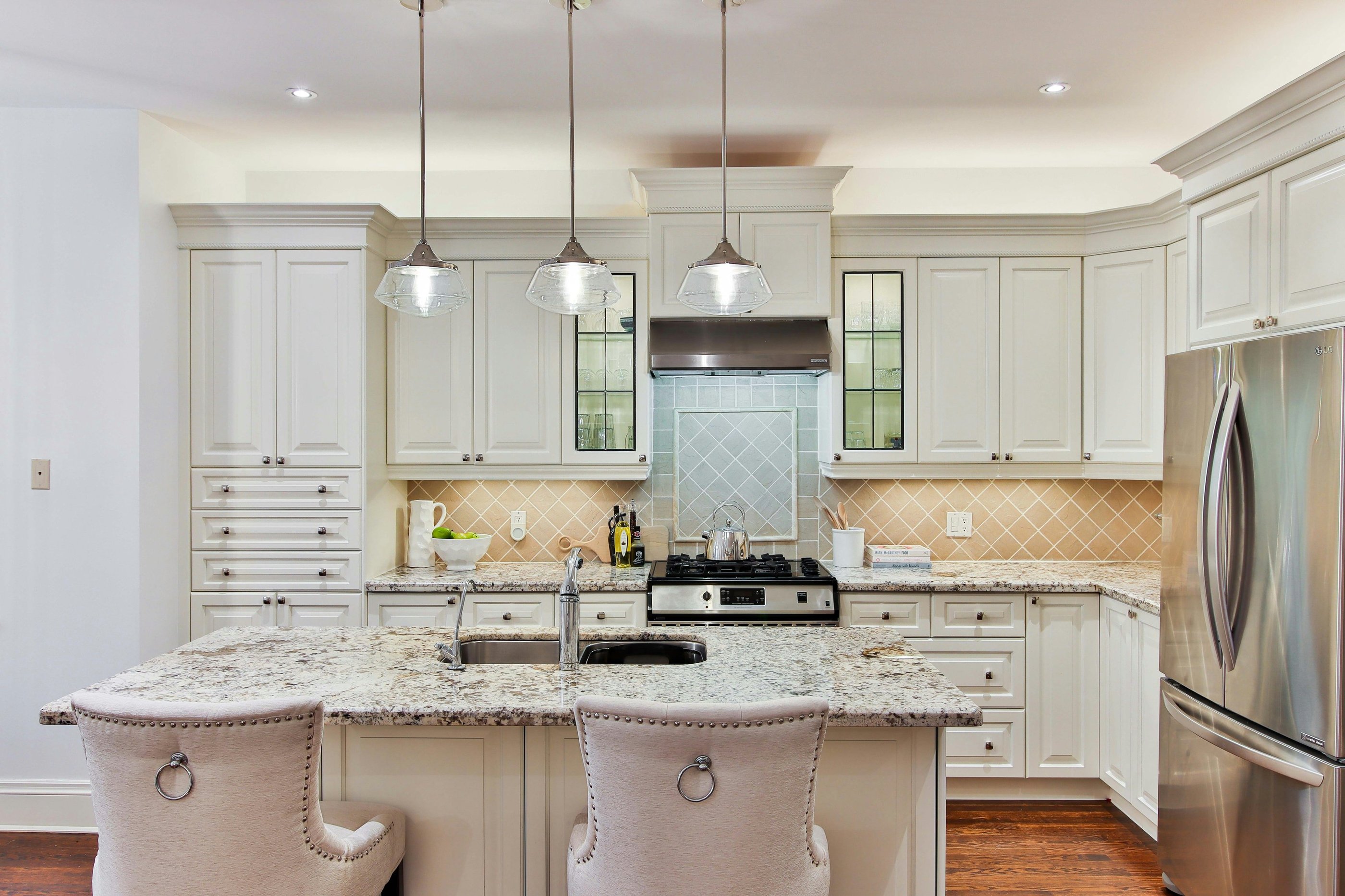 Luxury pastel and white tone kitchen. Light granite benchtops and a steel refrigerator.