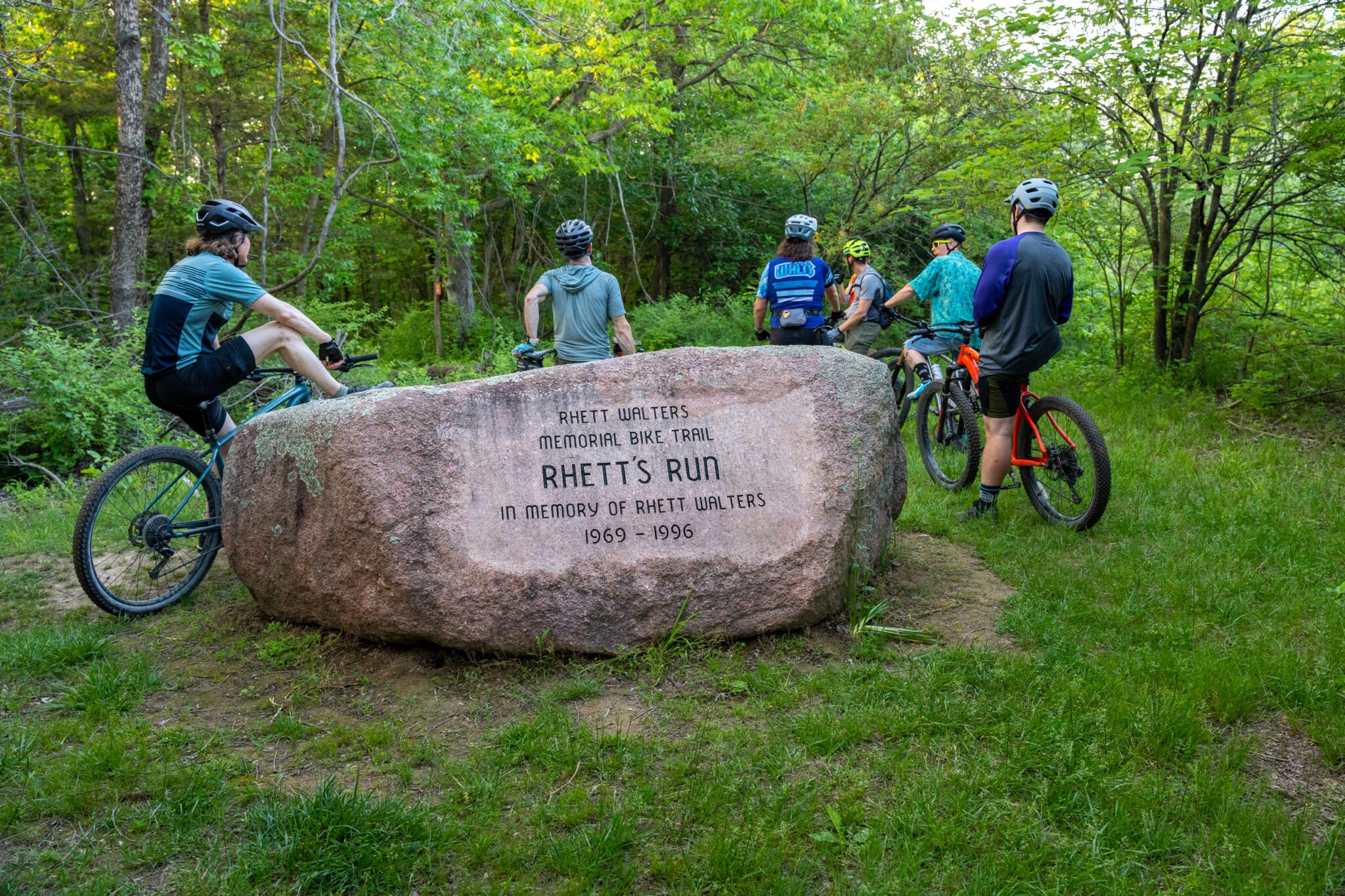 People stopped on their bikes next to a large rock engraved with the memorial info of "Rhett's Run"
